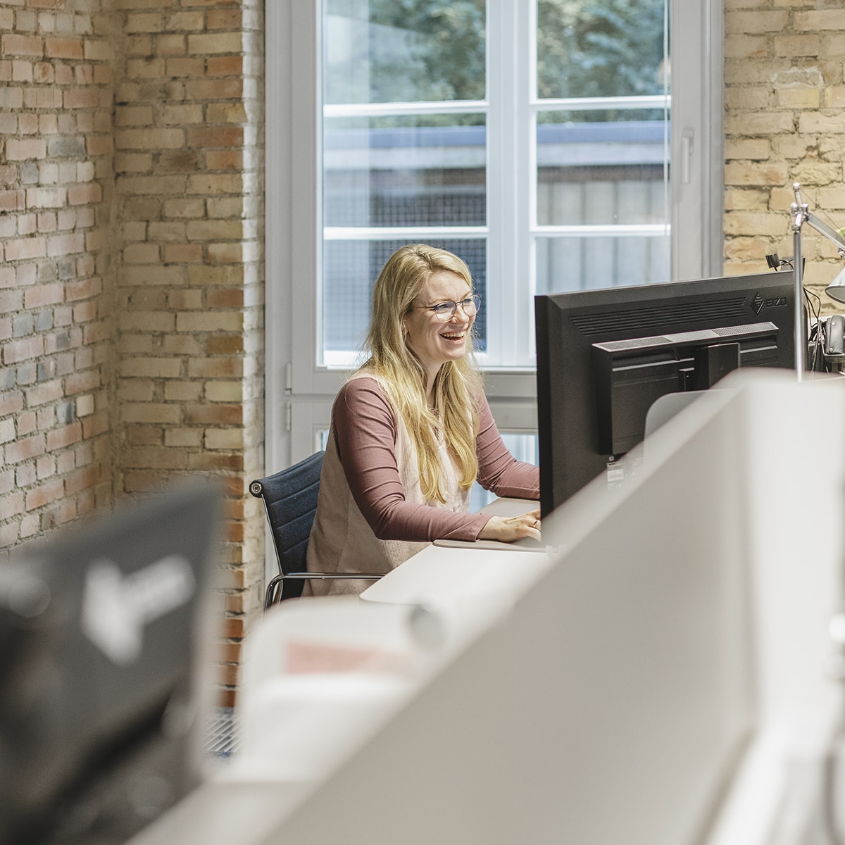 hochzwei-mitarbeitermotiv_M9A1996.jpg Mitarbeiterin des Teams Online Marketing bei HOCHZWEI lacht bei der Arbeit am Schreibtisch