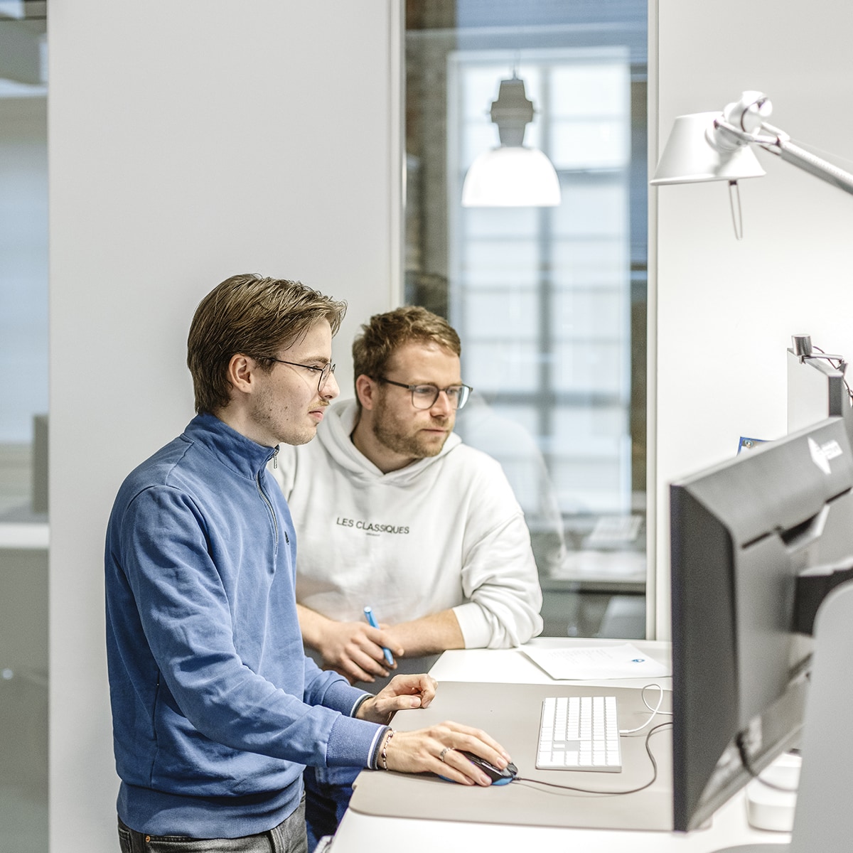 hochzwei-mitarbeitermotiv_M9A2060.jpg Ein Grafiker bespricht sich mit einem Kollegen an seinem Arbeitsplatz