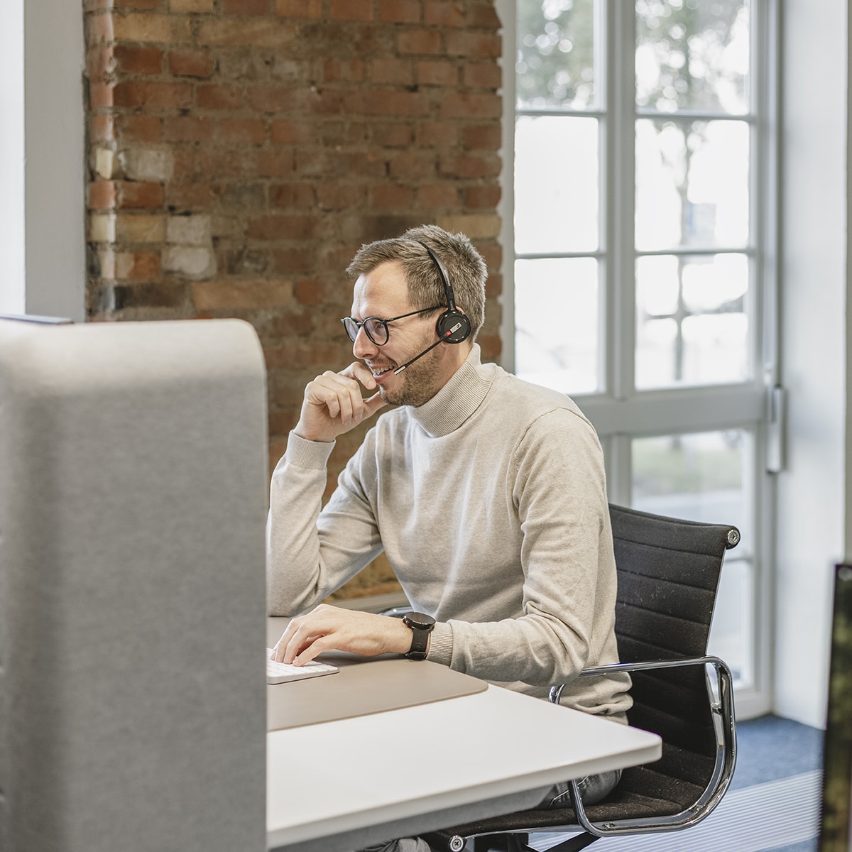 Ein Mitarbeiter von HOCHZWEI mit Headset sitzt an seinem Schreibtisch und lächelt