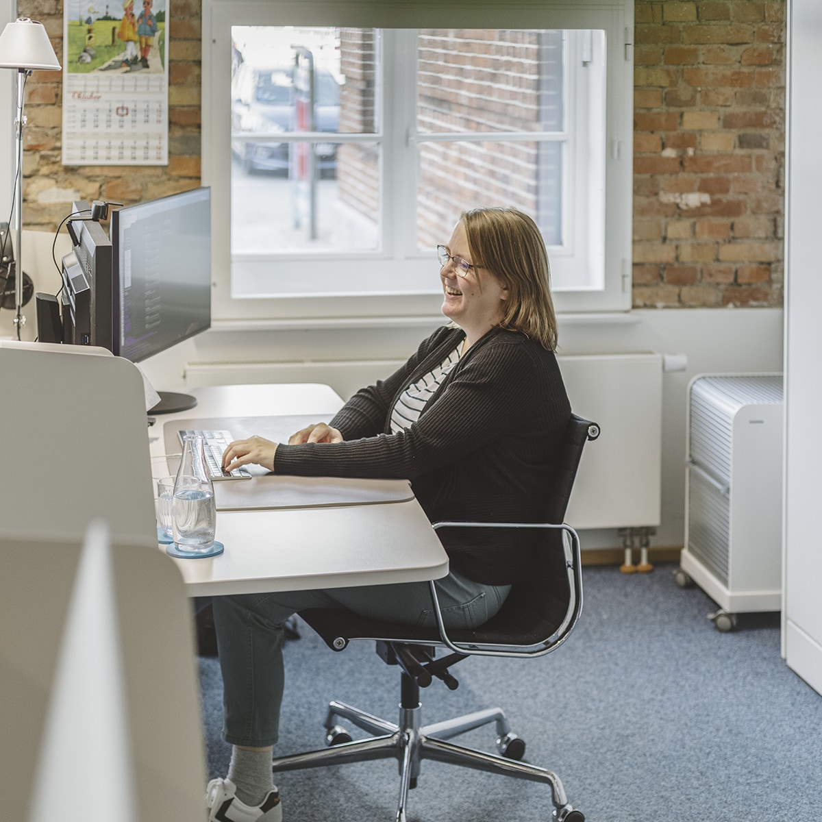 Mitarbeiterin von HOCHZWEI sitzt an ihrem Arbeitsplatz am Fenster
