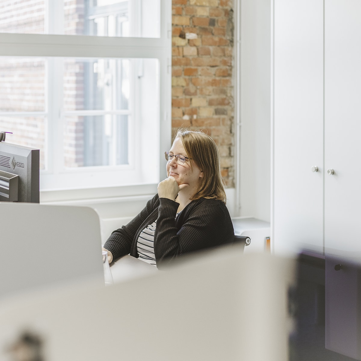 Mitarbeiterin von HOCHZWEI sitzt an ihrem Arbeitsplatz und überlegt