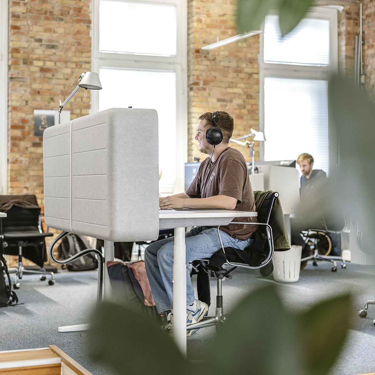 Mitarbeiter sitzt mit Kopfhörern am Arbeitsplatz