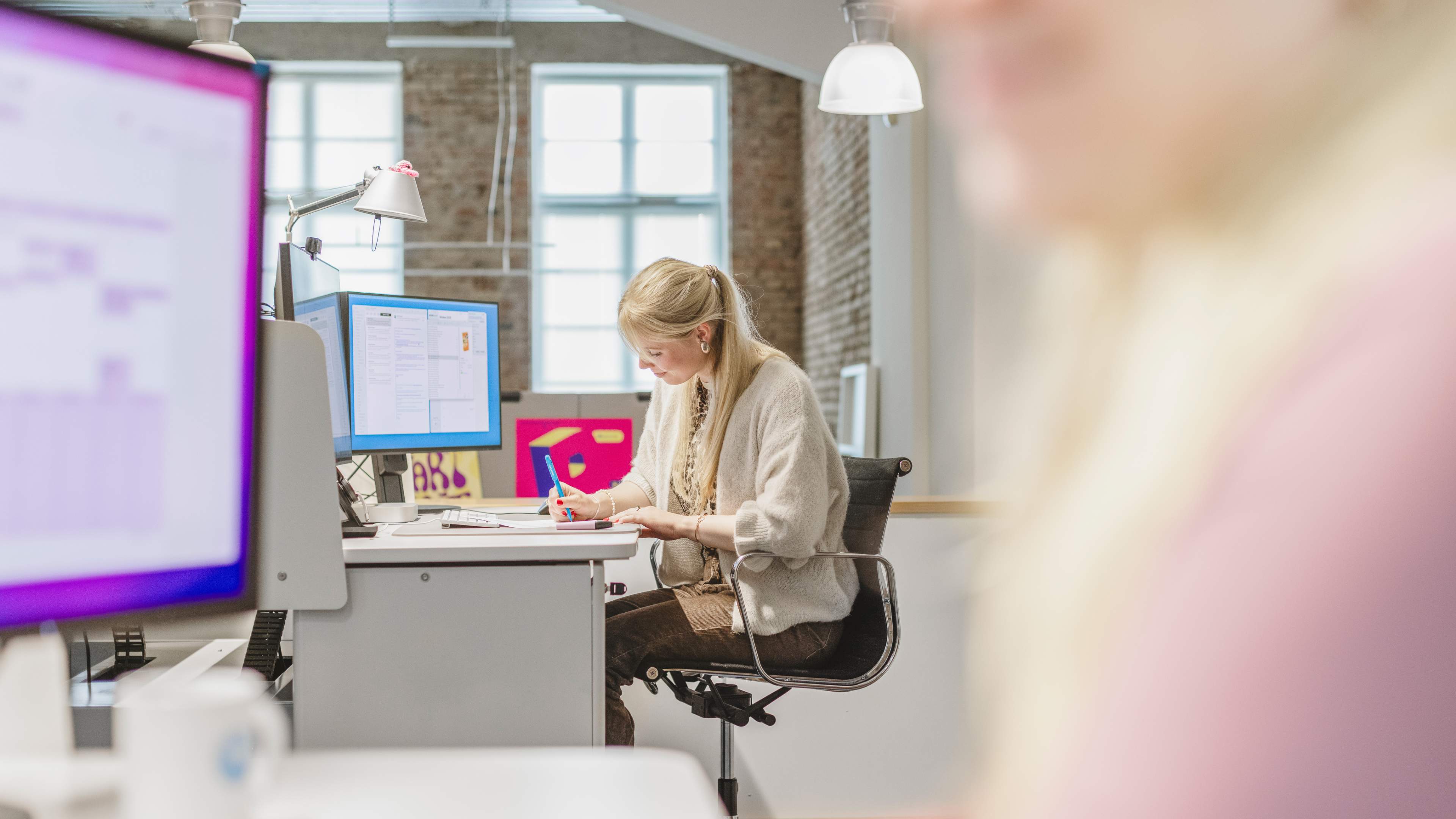 Mitarbeiterin von HOCHZWEI sitzt an ihrem Arbeitsplatz und liest etwas Ausgedrucktes auf ihrem Schreibtisch