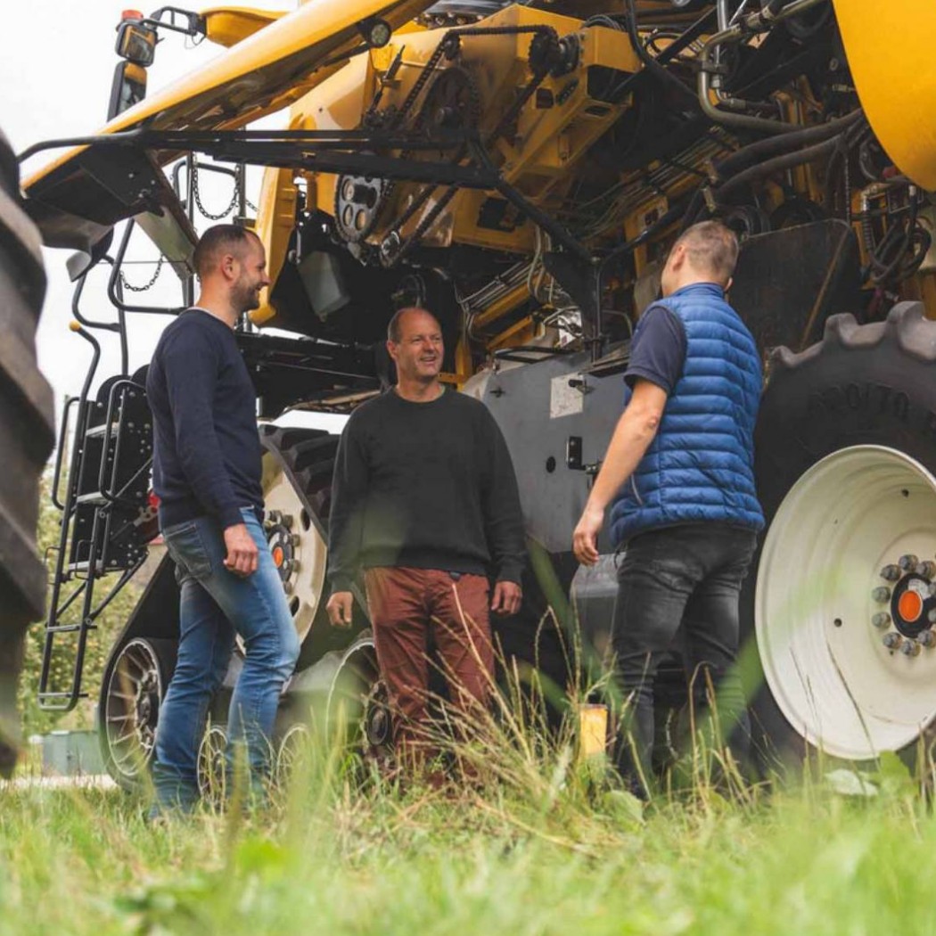 Drei Männer stehen vor einem Mähdrescher und unterhalten sich