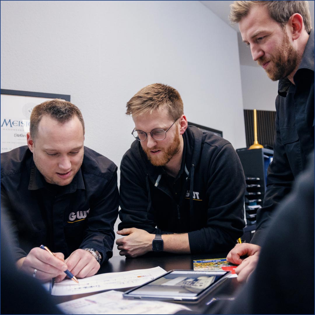 hochzwei_Internetauftritt_GWT_teaser_03.jpg Drei Handwerker sind an einem Tisch versammelt und lesen ein Blatt Papier
