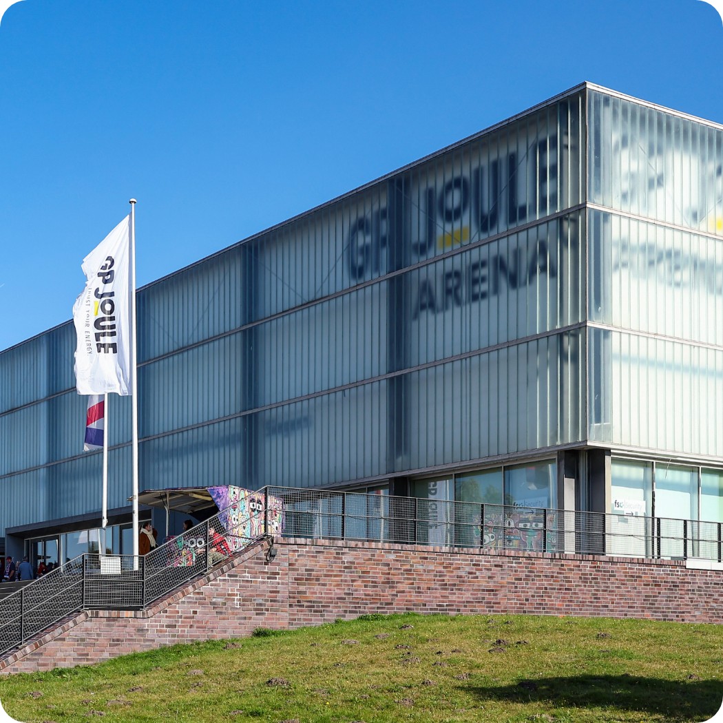 Graue GP Joule Arena, davor eine Flagge mit dem GP Joule Logo auf grünem Rasen