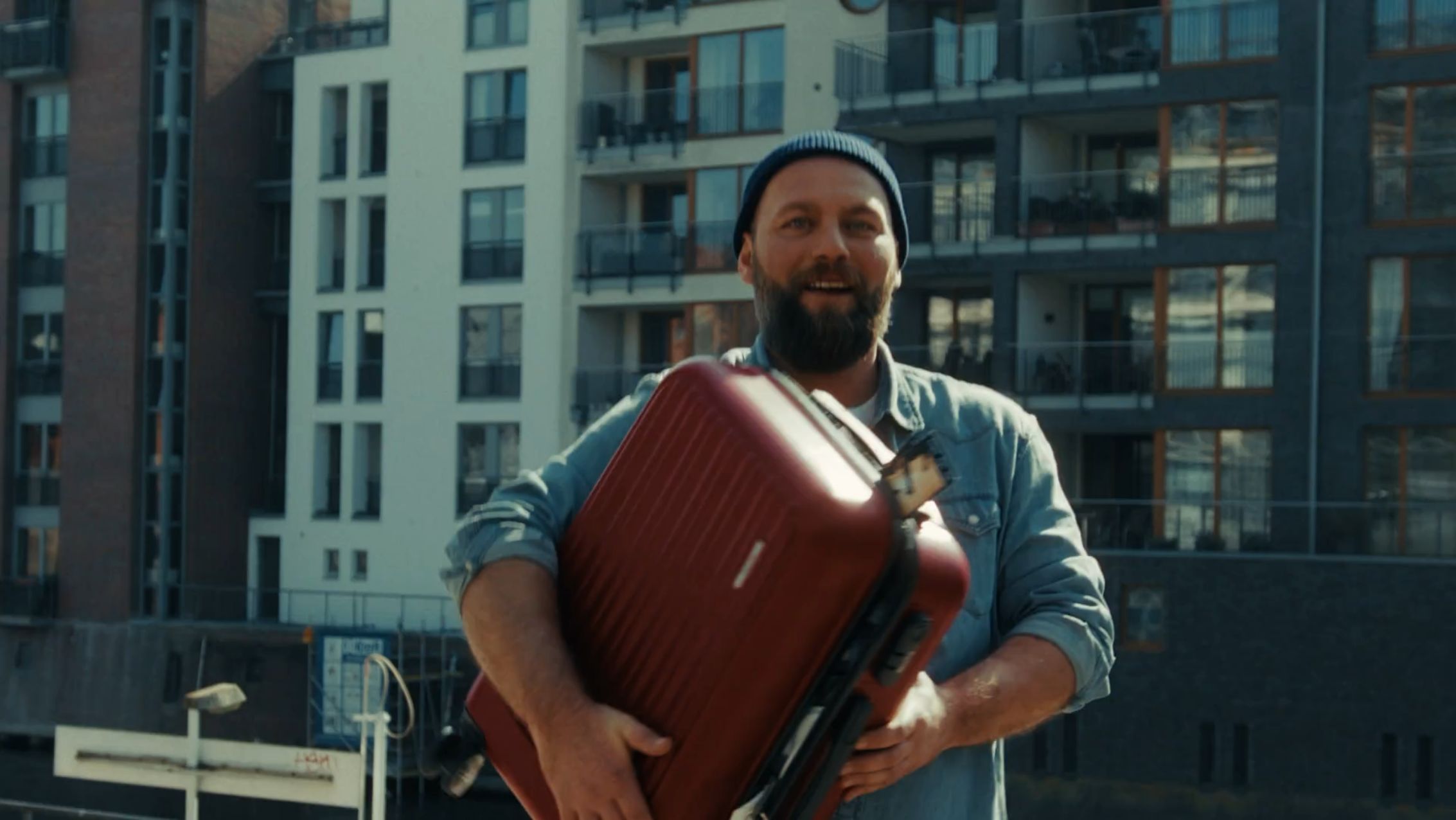 Mann mit Wollmütze und großem Koffer unter dem Arm.