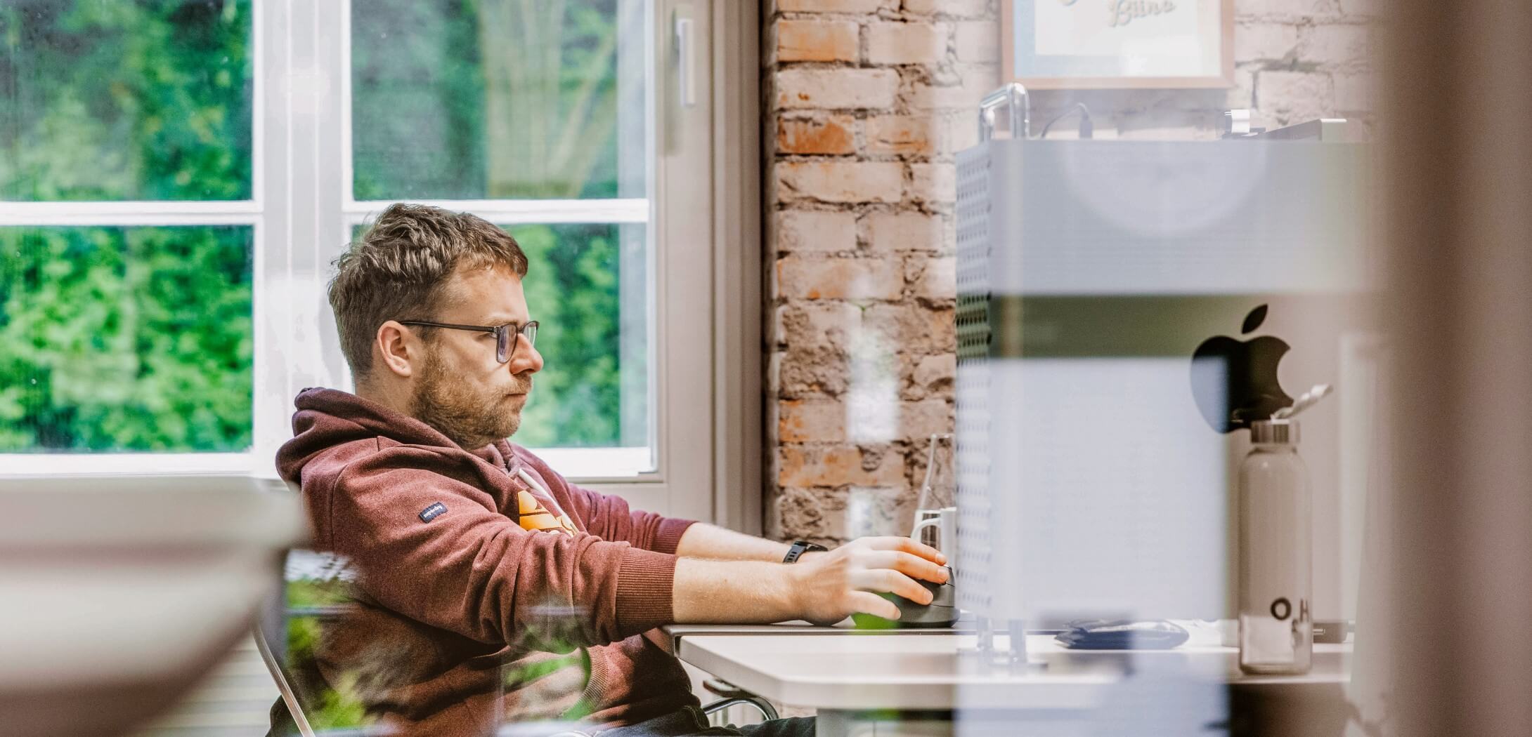 h2_crefozert_teaser_02.jpg Ein Hochzwei Mitarbeiter in einem braunen Kapuzenpullover arbeitet konzentriert an einem Schreibtisch.