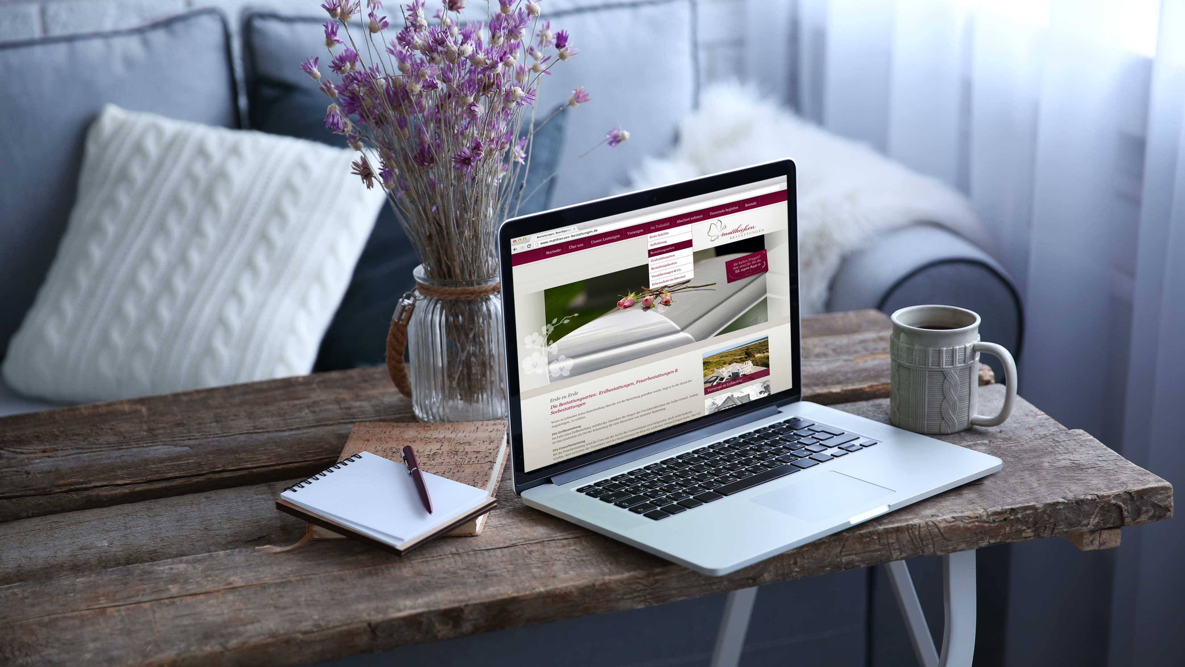 hochzwei_mabe_slider_03.jpg Graues Sofa mit einem Couchtisch aus Holz auf dem ein Laptop steht