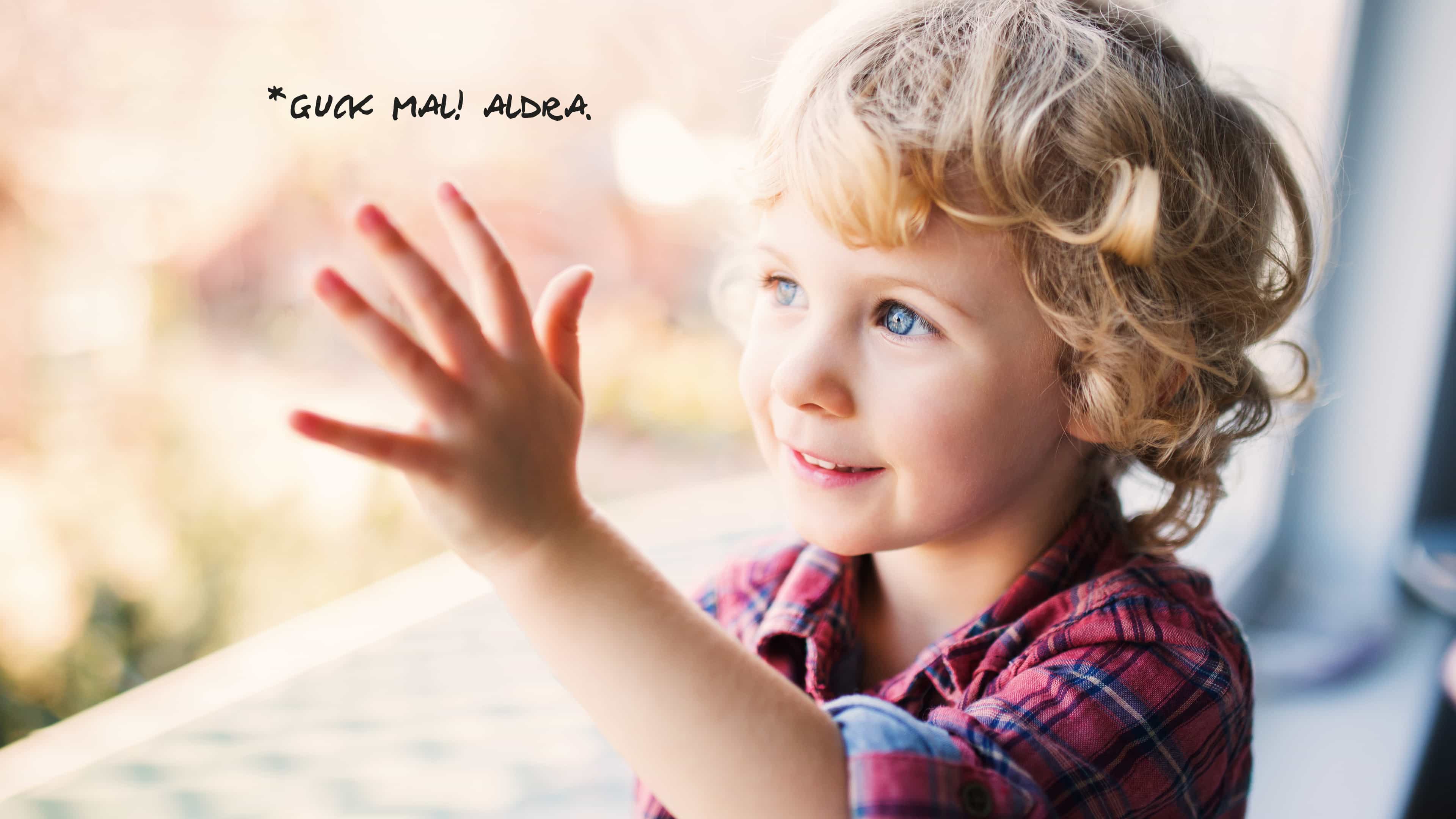 Kleiner blonder Junge berührt Fenster, darauf steht Guck mal, Aldra