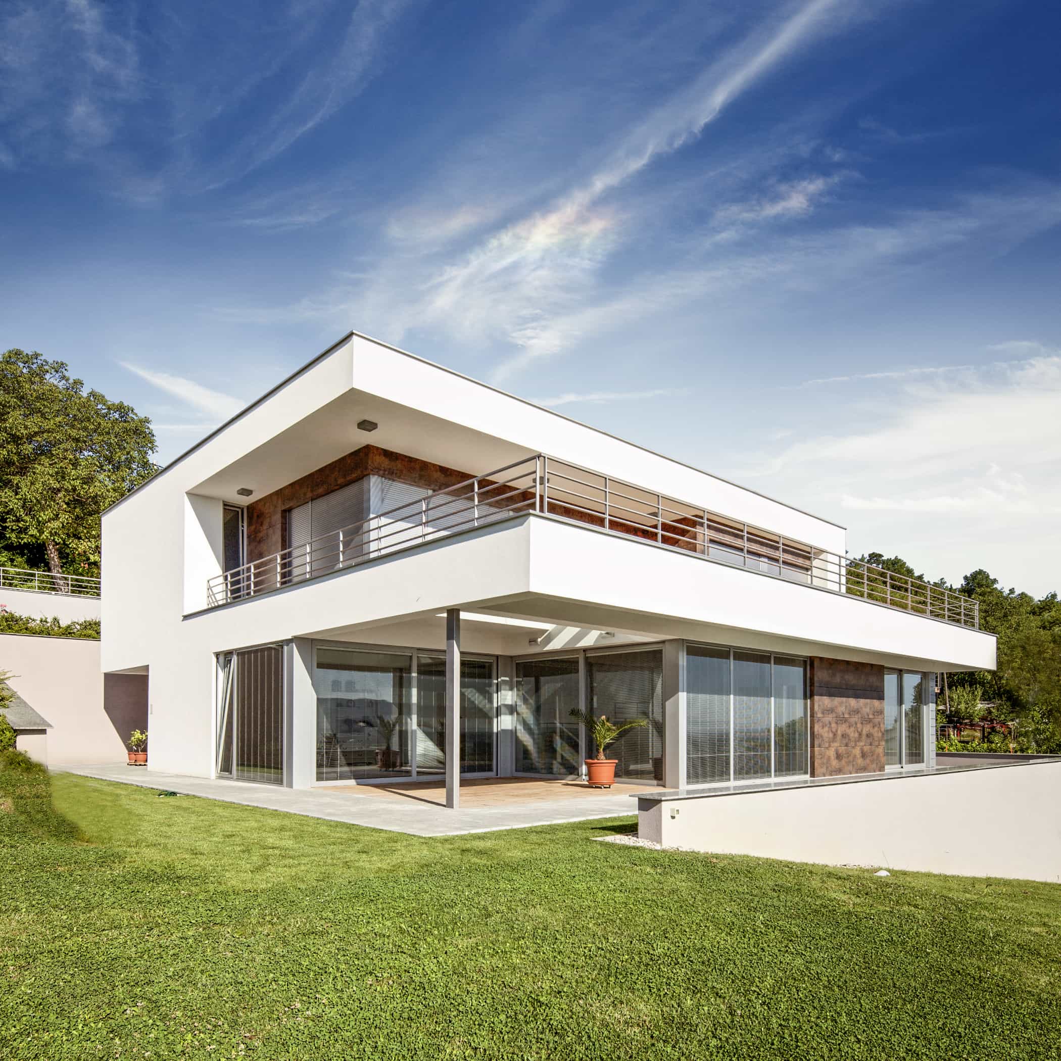 Modernes weißes Haus mit grünem Rasen davor und blauem Himmel
