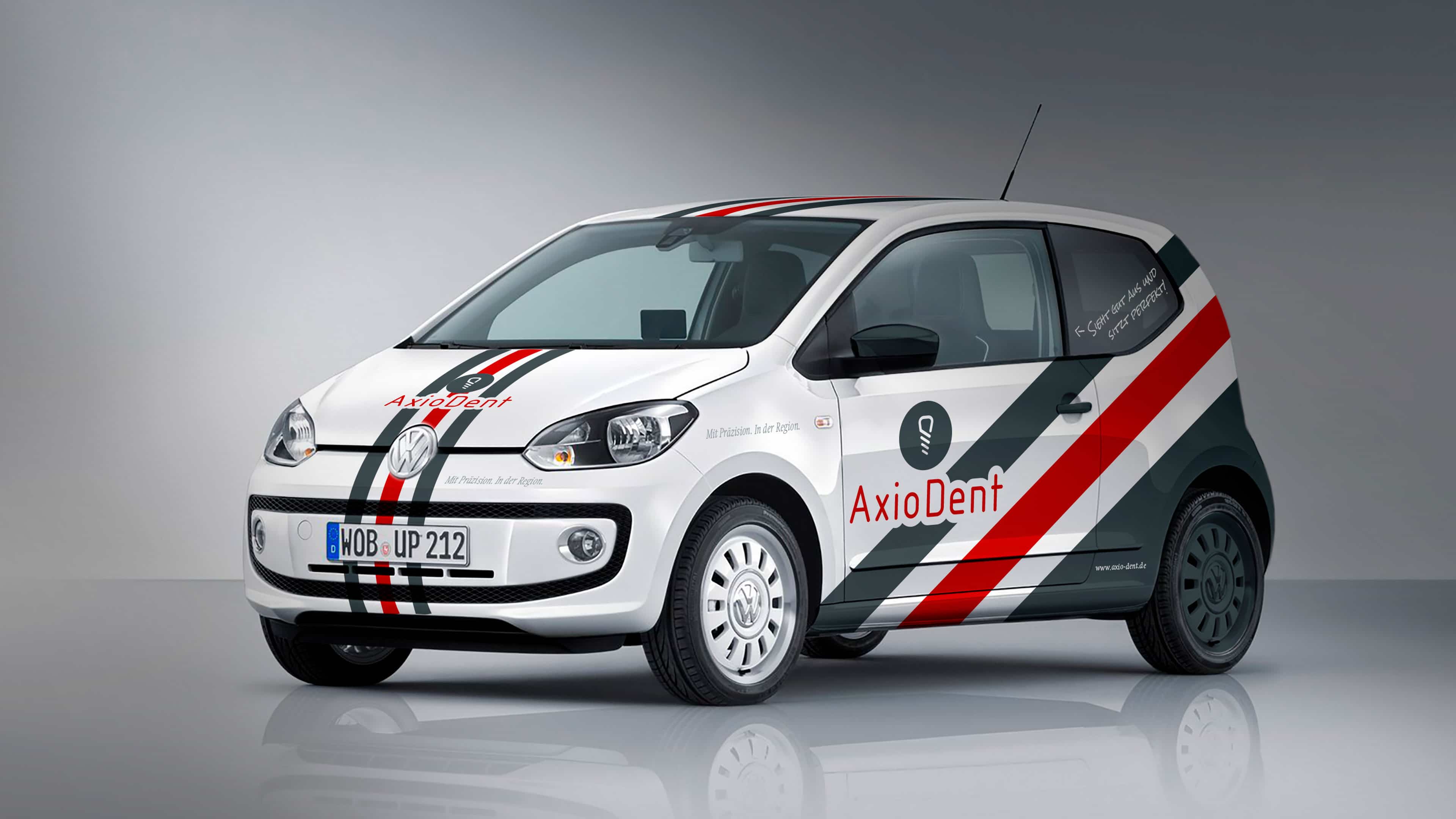 hochzwei_axiodent_slider_01.jpg Ein mit AxioDent-Logo und rot-grauen Streifen beklebter weißer VW Up von schräg vorne