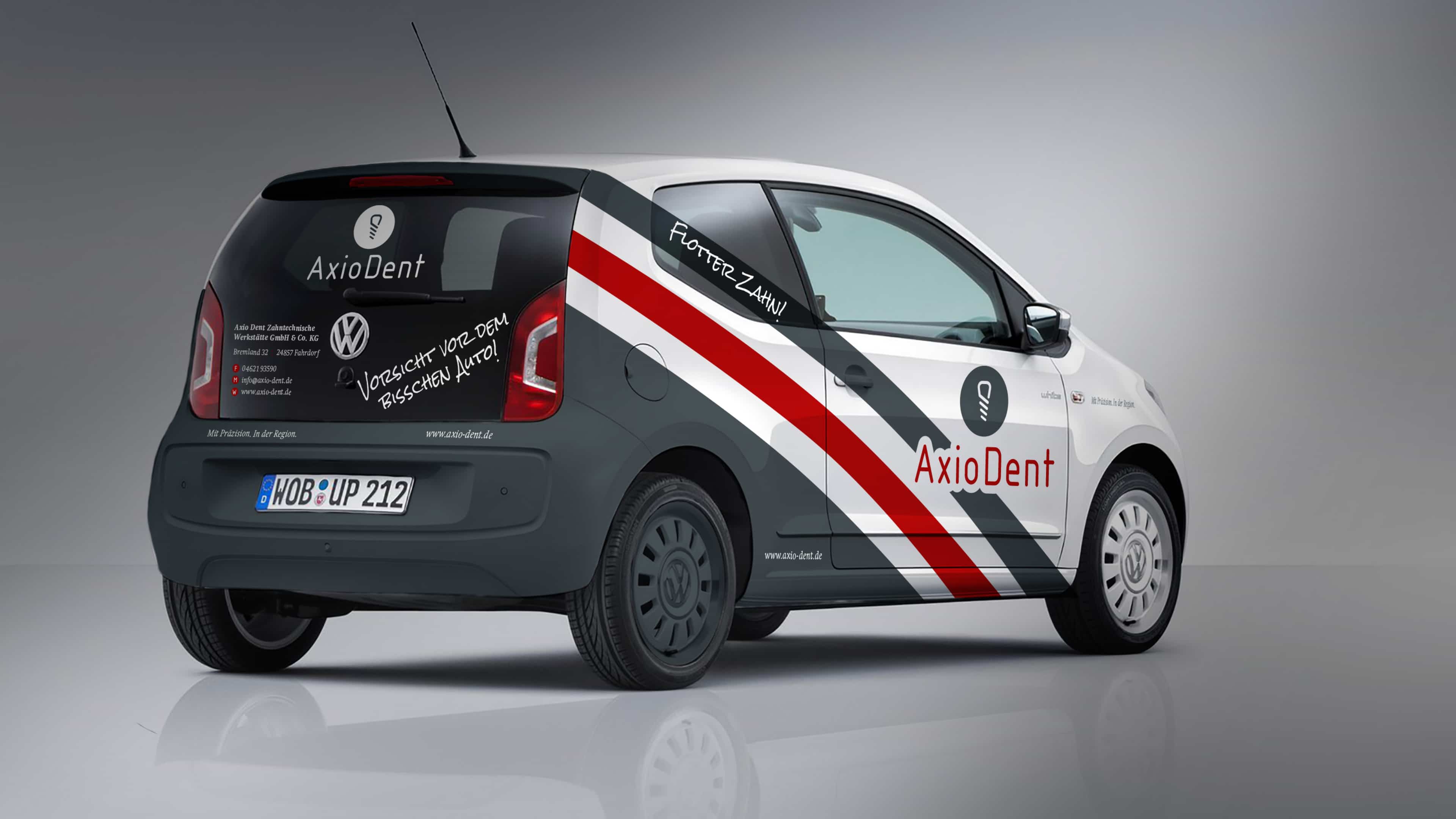 hochzwei_axiodent_slider_03.jpg Ein mit AxioDent-Logo und rot-grauen Streifen beklebter VW Up von schräg hinten