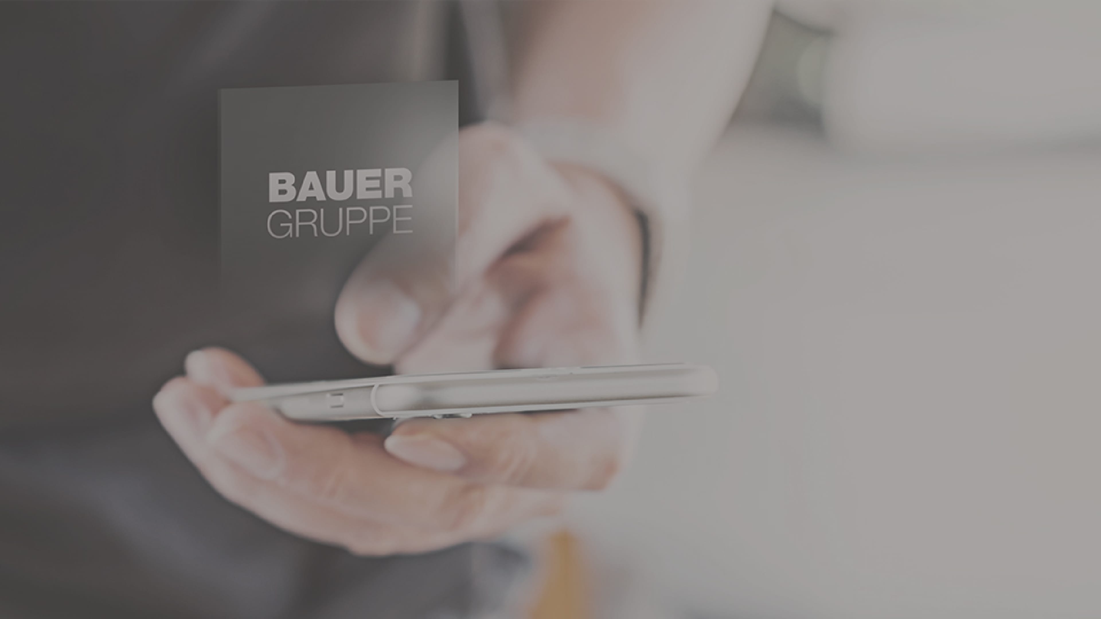 Hand hält Smartphone, zu sehen ist das Logo der BAUER GRUPPE
