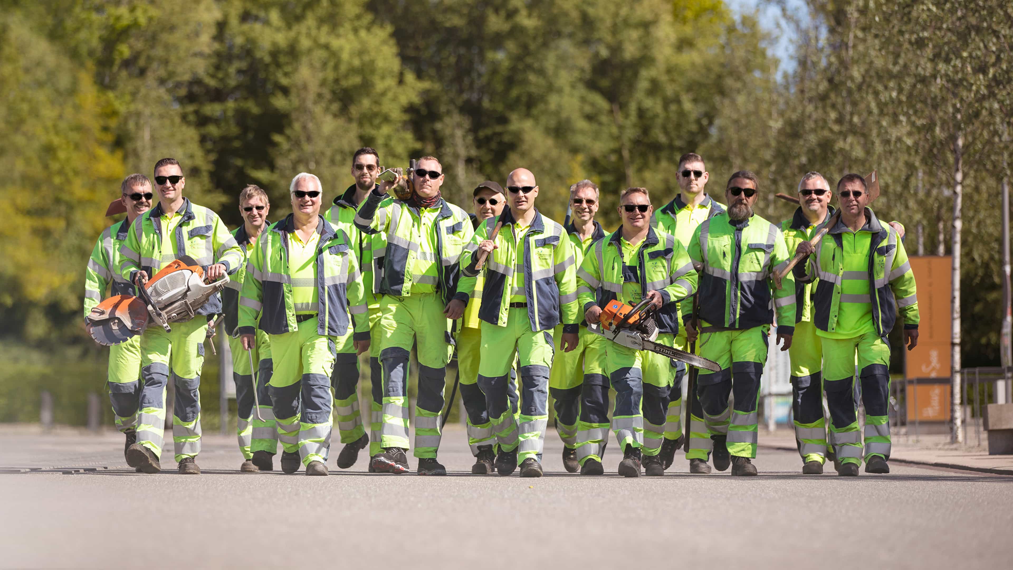 Vierzehn Mitarbeiter im gelben Arbeitsanzügen mit Werkzeugen und Sonnenbrillen
