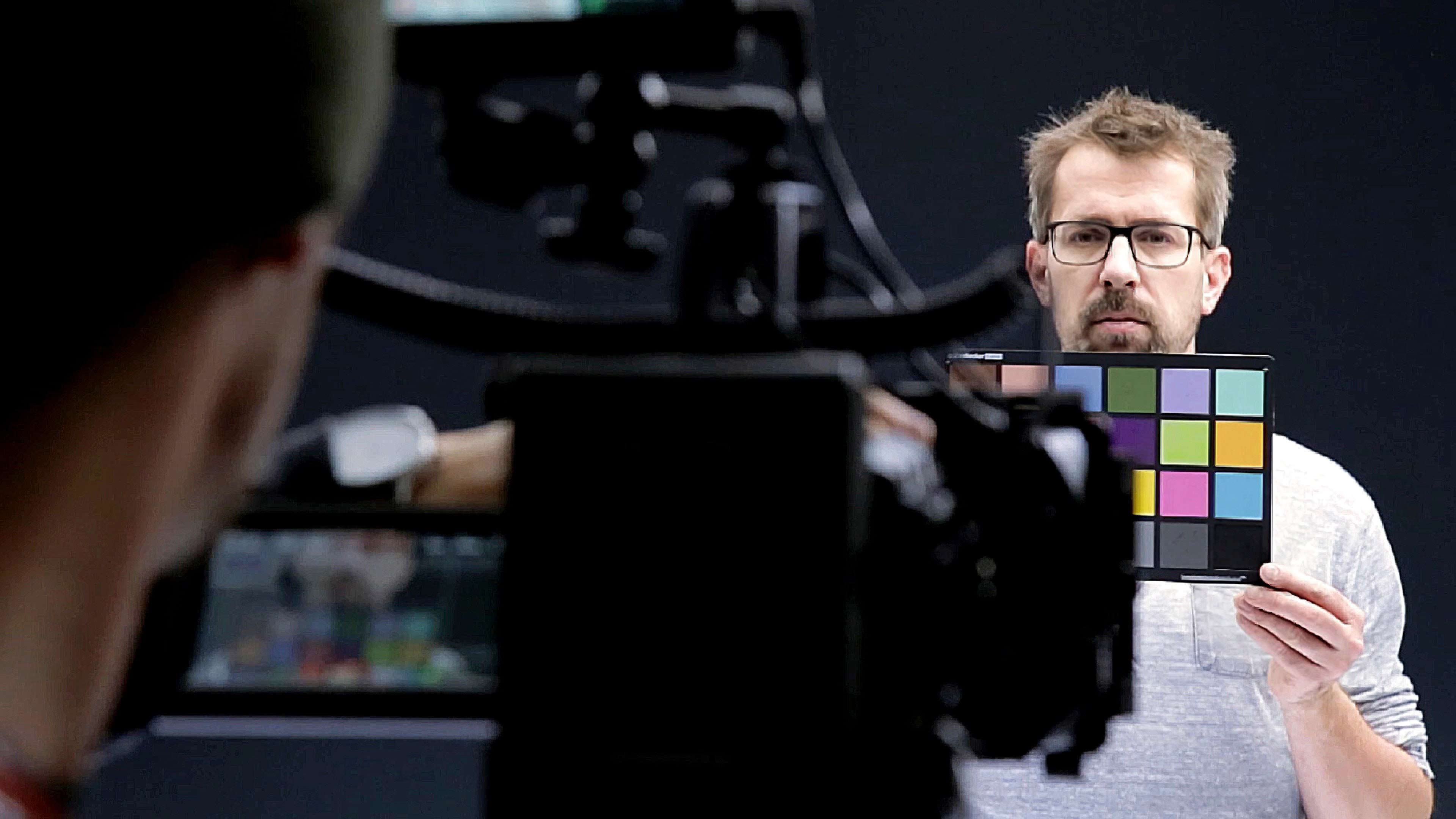 hochzwei_bb_slider_02.jpg Mann mit Brille hält Farbtafel in die laufende Kamera