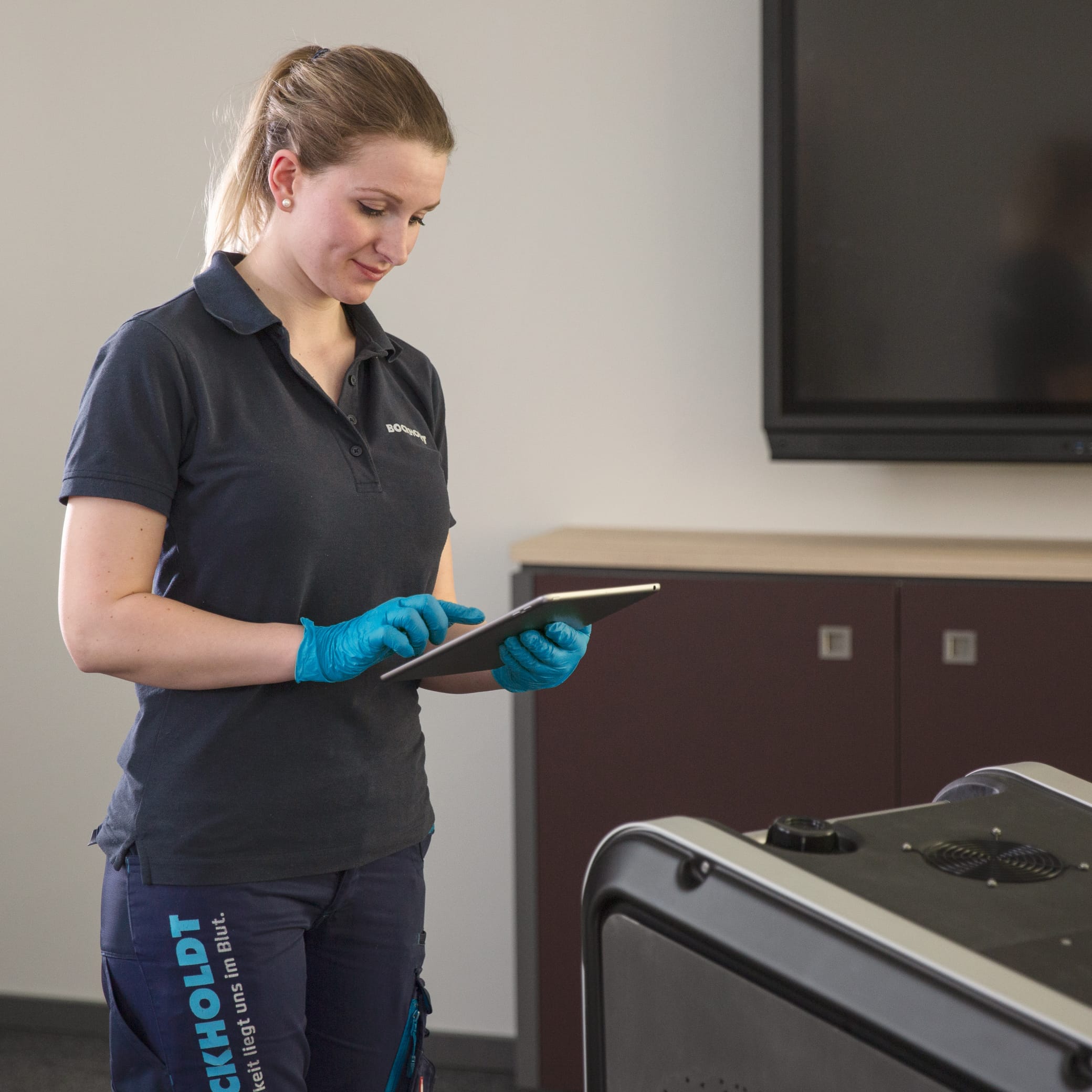 hochzwei_bockh_teaser_06.jpg Frau im Polohemd und Gummihandschuhen schaut auf ein Tablet