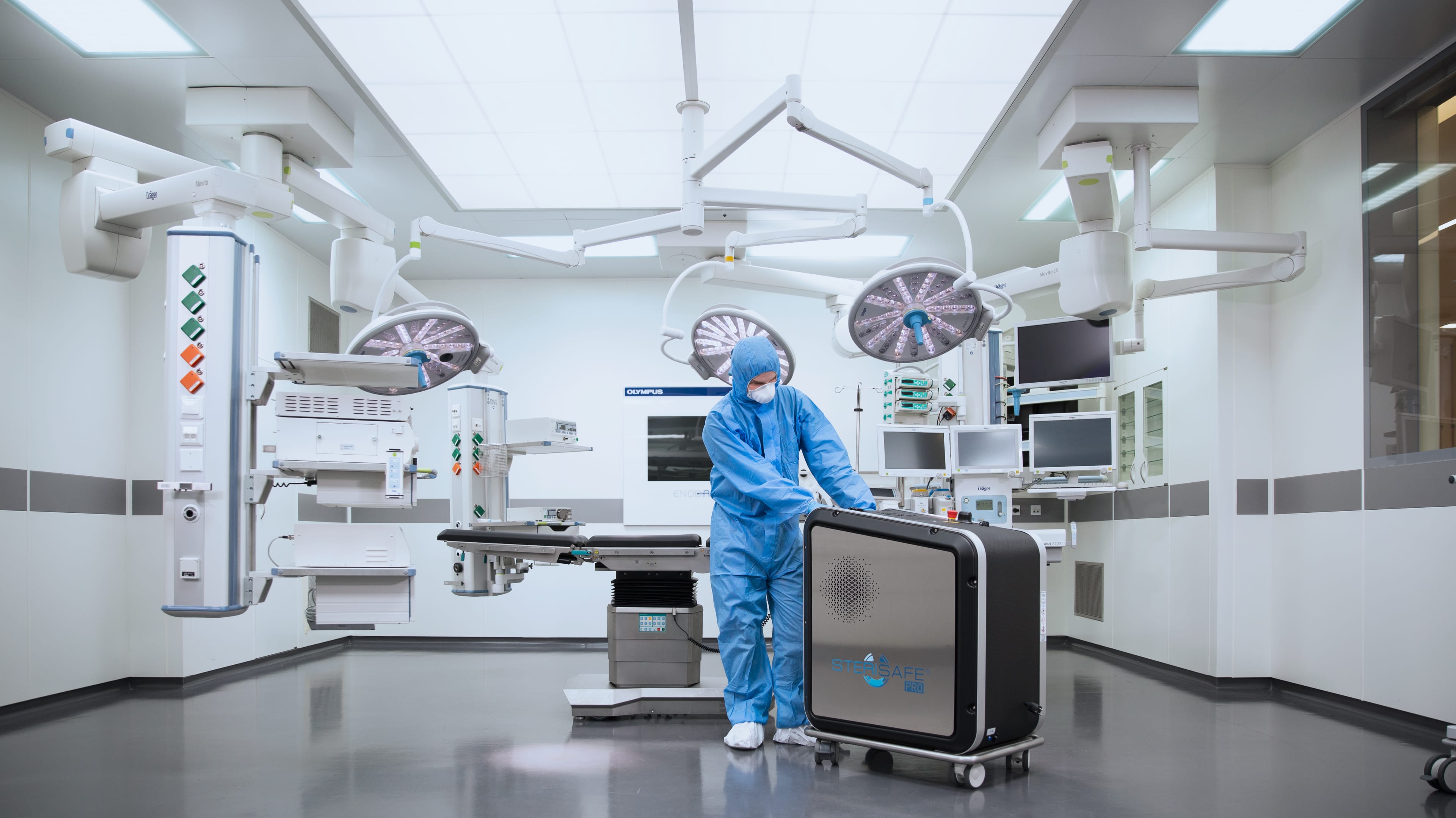 Person im blauen Ganzkörperanzug steht im leeren OP-Saal