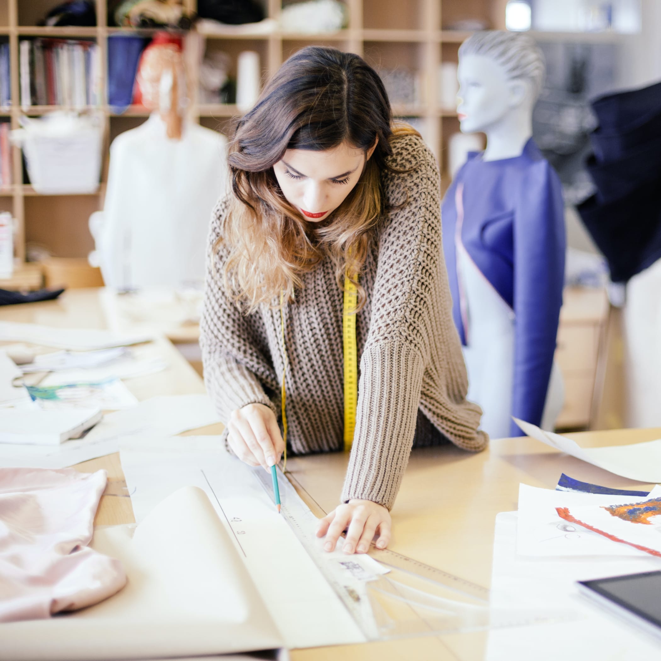 hochzwei_cjs_teaser_02.jpg Langhaarige Schneiderin zeichnet mit Lineal und Bleistift auf einem Blatt Papier