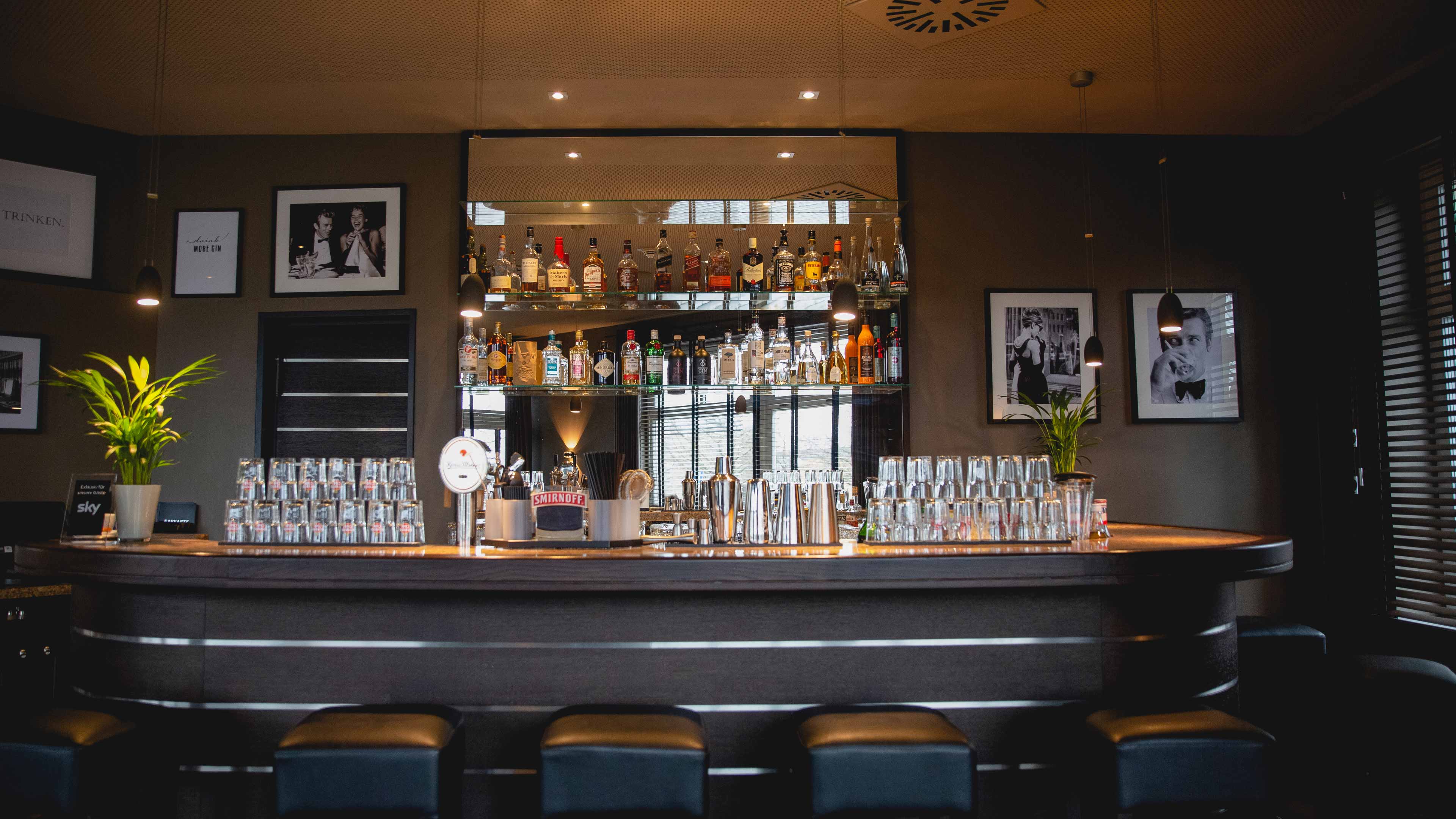 hochzwei_congar_slider_03.jpg Frontaler Blick auf schwarze Hotelbar mit Alkoholflaschen auf Wandregal