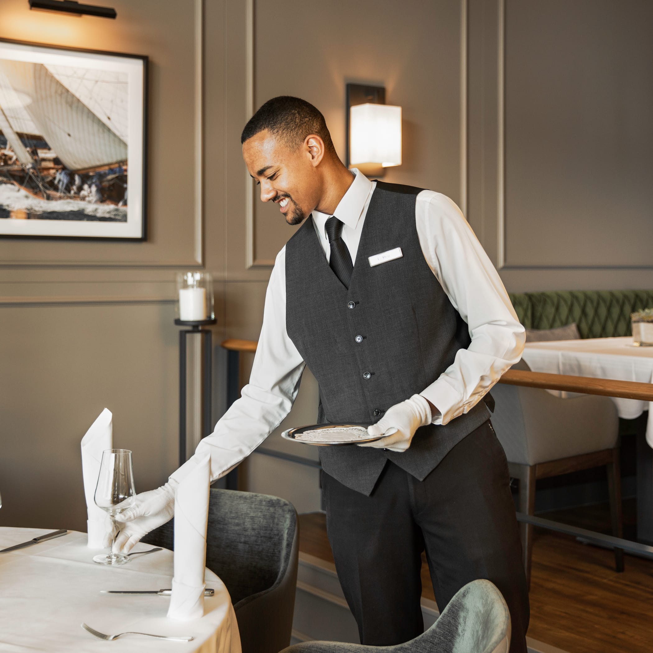 hochzwei_congar_teaser_03.jpg Lächelnder Kellner mit weißen Handschuhen deckt einen Tisch mit Weingläsern