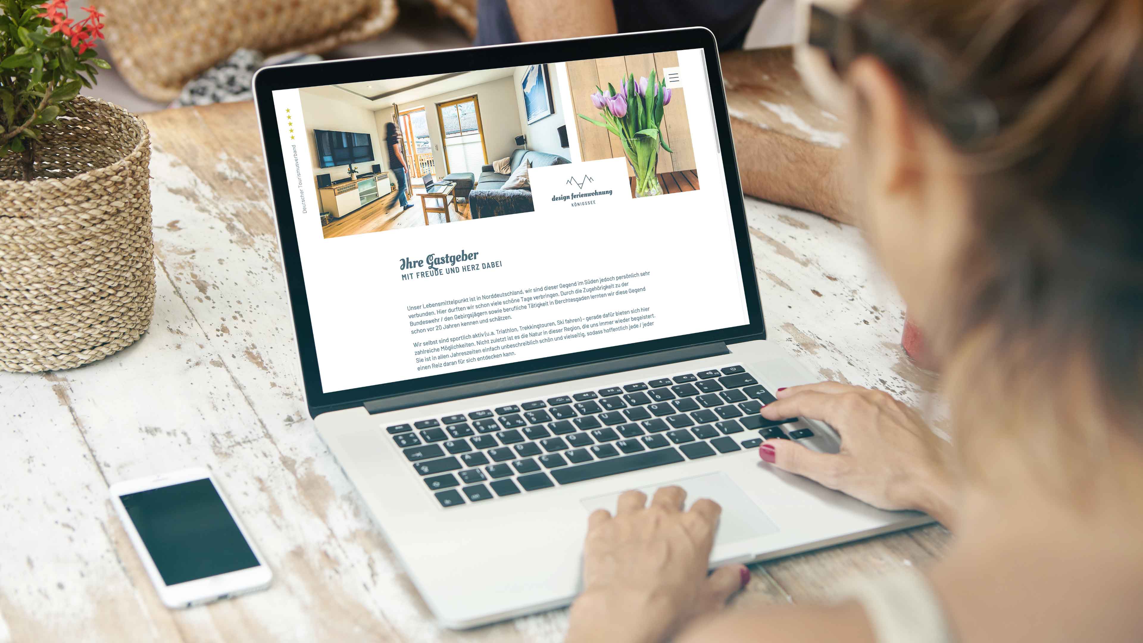 Blick über die Schulter einer Frau am Laptop, das die Website von design fewo Königssee über Gastgeber zeigt