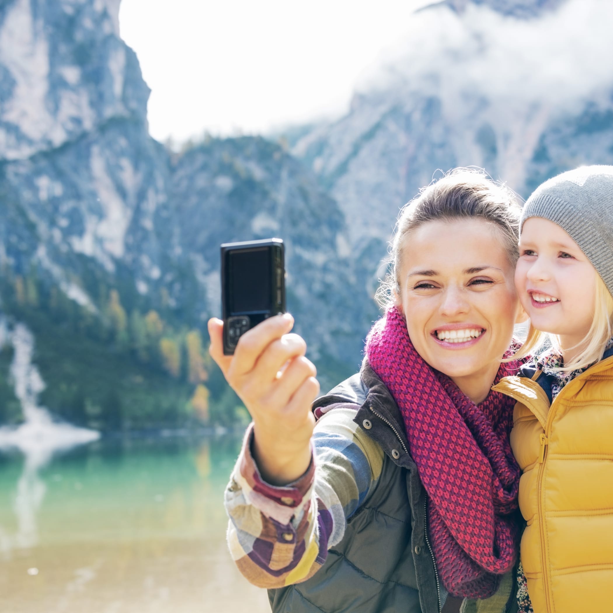 hochzwei_fwschoen_teaser_06.jpg Lächelnde Frau und Kind machen ein Selfie vor einem Bergsee