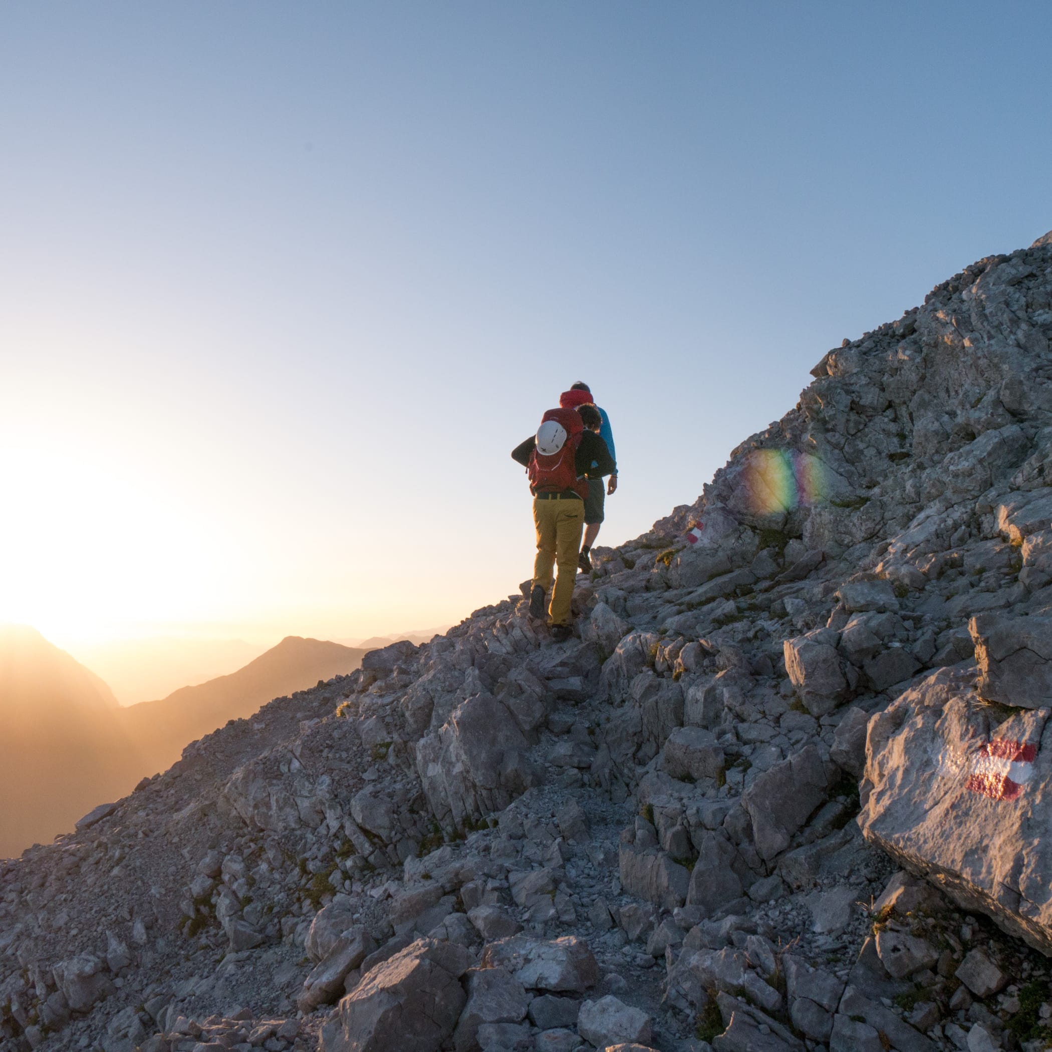 hochzwei_fwschoen_teaser_09.jpg Zwei Bergsteiger von hinten auf einem felsigen Berg vor blauem Himmel