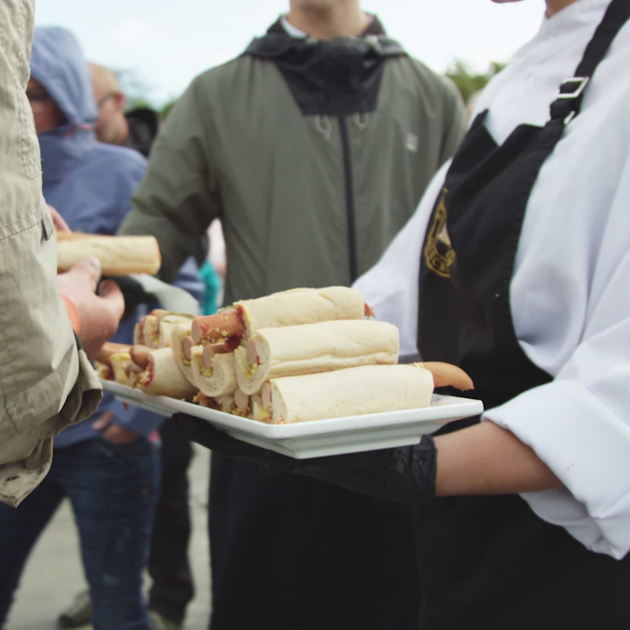hochzwei_sfdw_teaser_04.jpg Koch verteilt Hotdogs auf einem Teller an Passanten