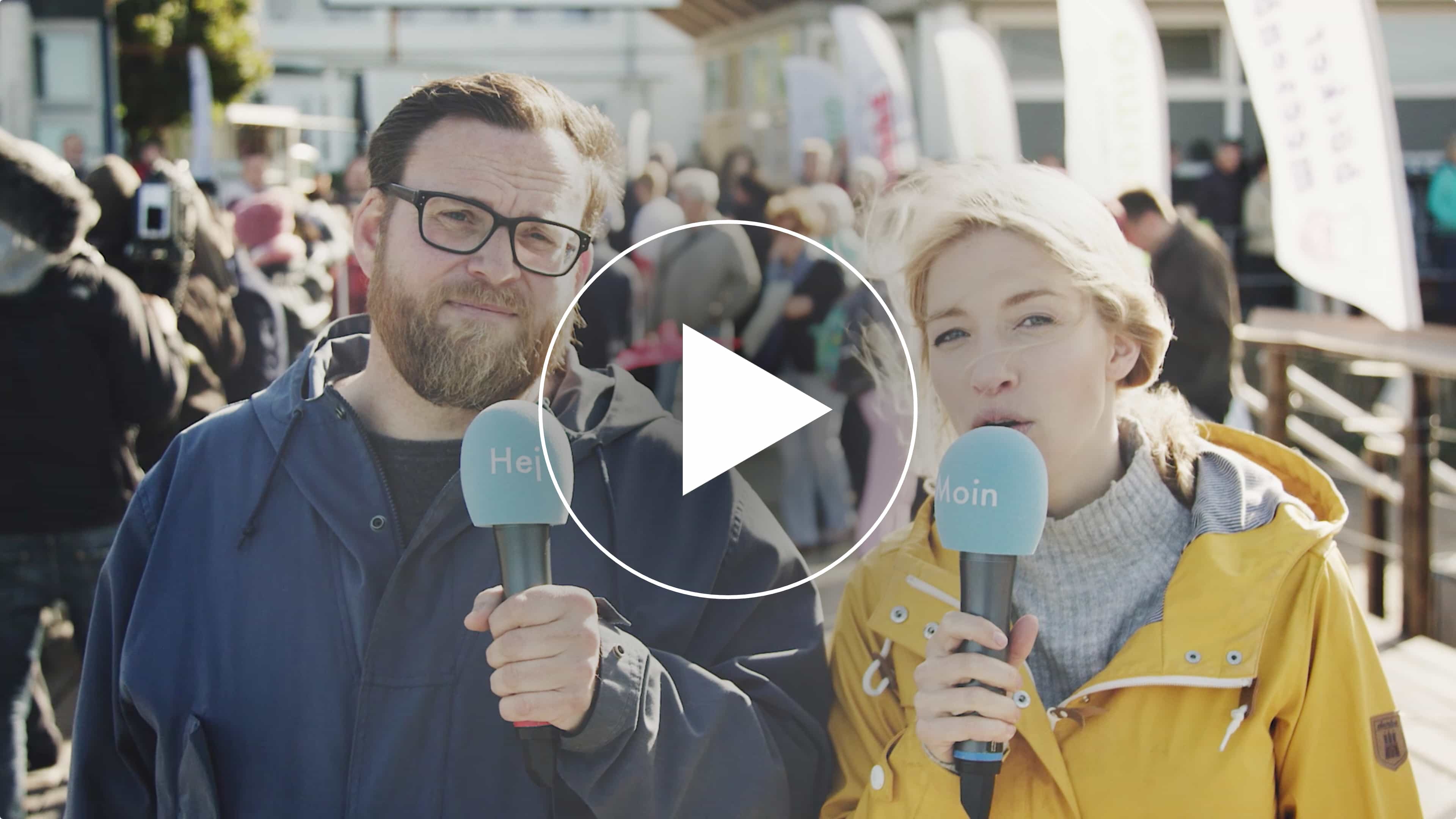 hochzwei_sfdw_video.jpg Reporter Malin und Daniel mit Mikrofonen auf denen Hej und Moin steht