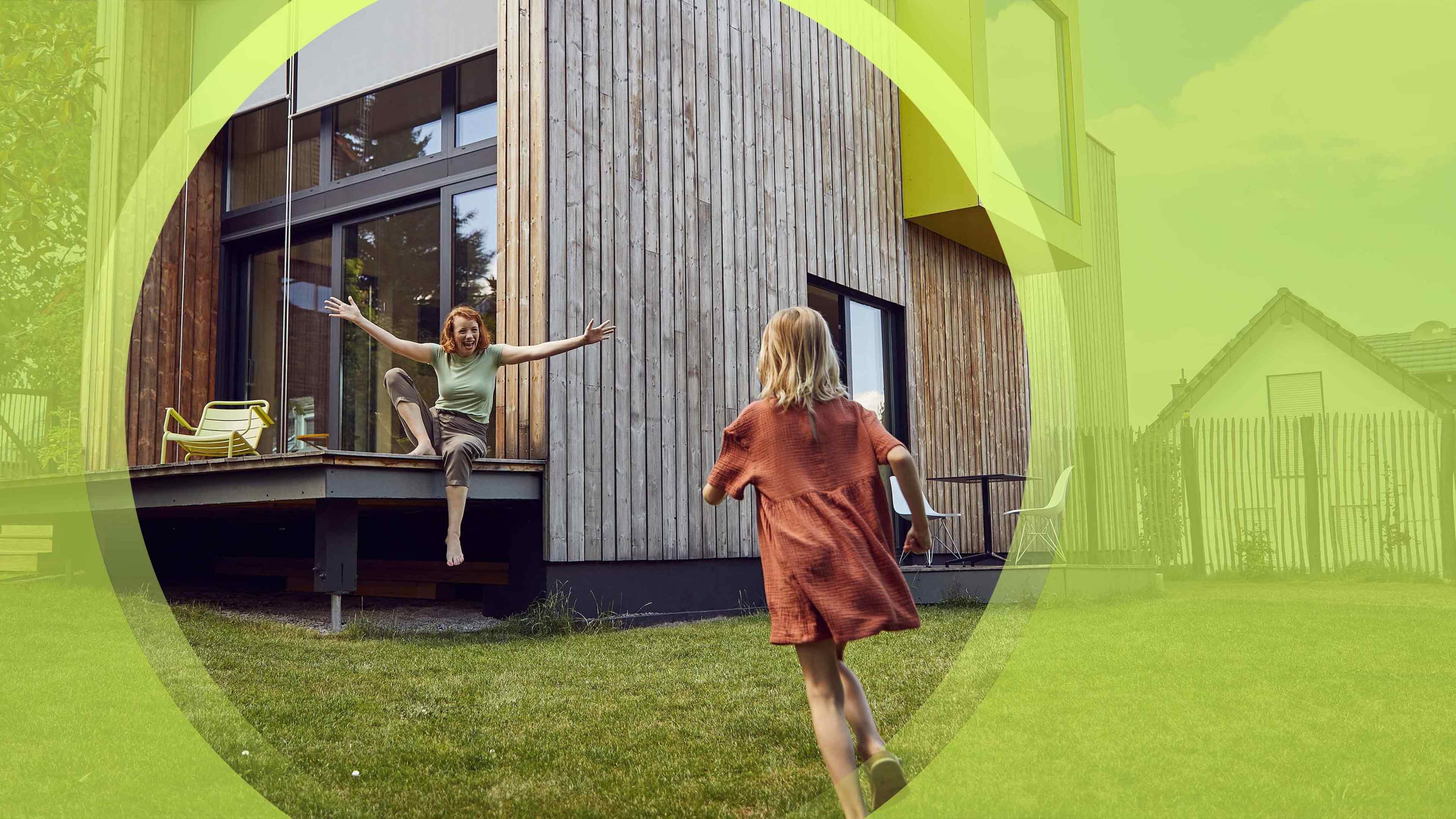 Kleines Kind rennt vor Holzhaus auf Frau mit ausgebreiteten Armen zu