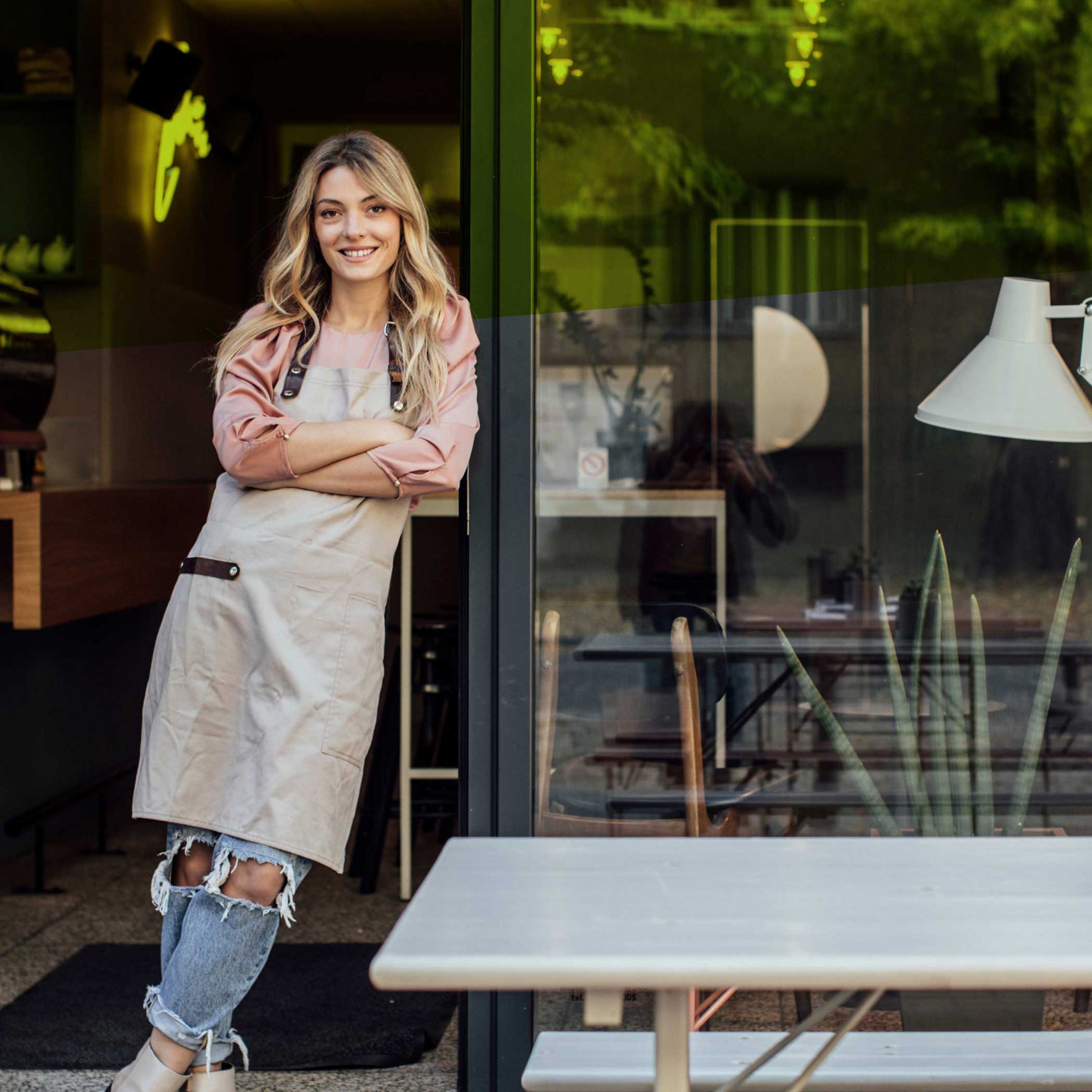 hochzwei_domcura_teaser_07.jpg Blondine mit Schürze lehnt an offener Terrassentür