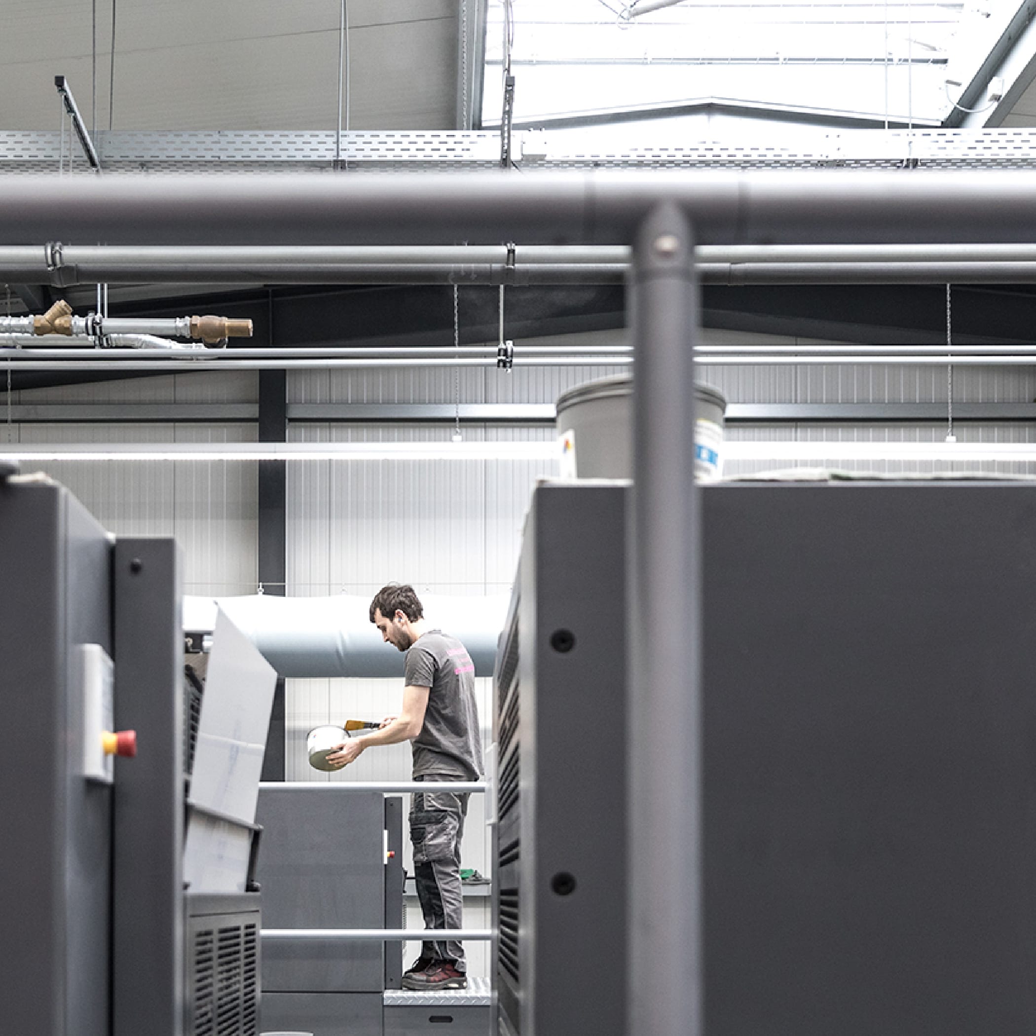 hochzwei_drle_teaser_06.jpg Blick durch Druckmaschinen auf einen männlichen Mitarbeiter, der mit Farbe hantiert