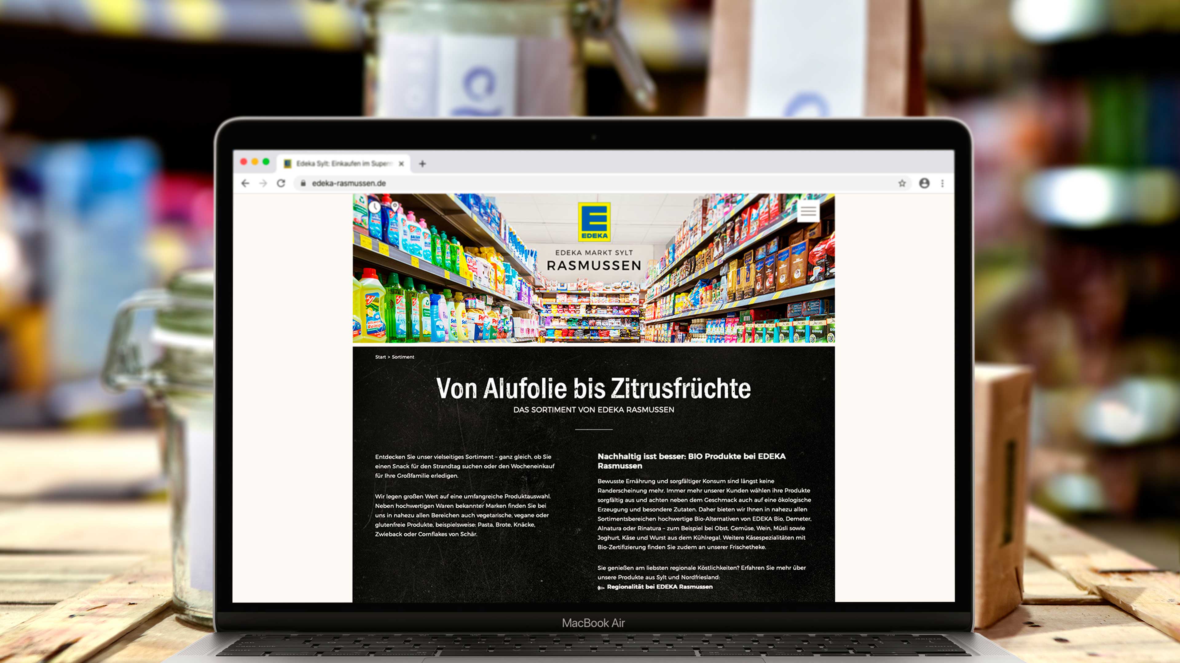 hochzwei_edra_slider_02.jpg Laptop zeigt Website edeka-rasmussen.de mit Text "Von Alufolie bis Zitrusfrüchte"
