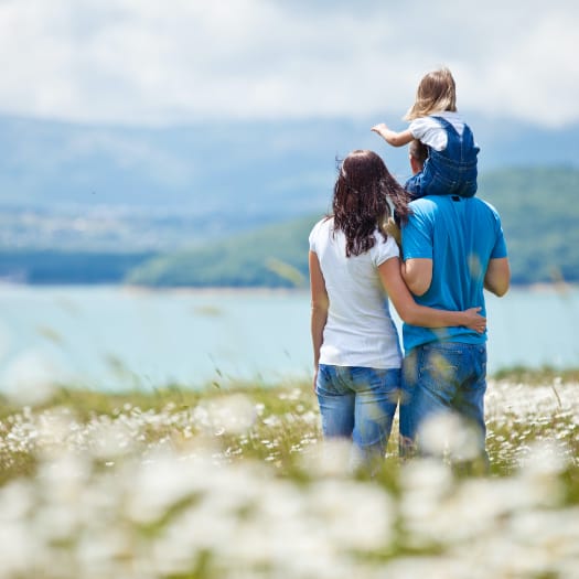 hochzwei_egeb_teaser_05.jpg Pärchen von hinten steht sich umarmend am Wasser, der Mann hat ein Kleinkind auf den Schultern