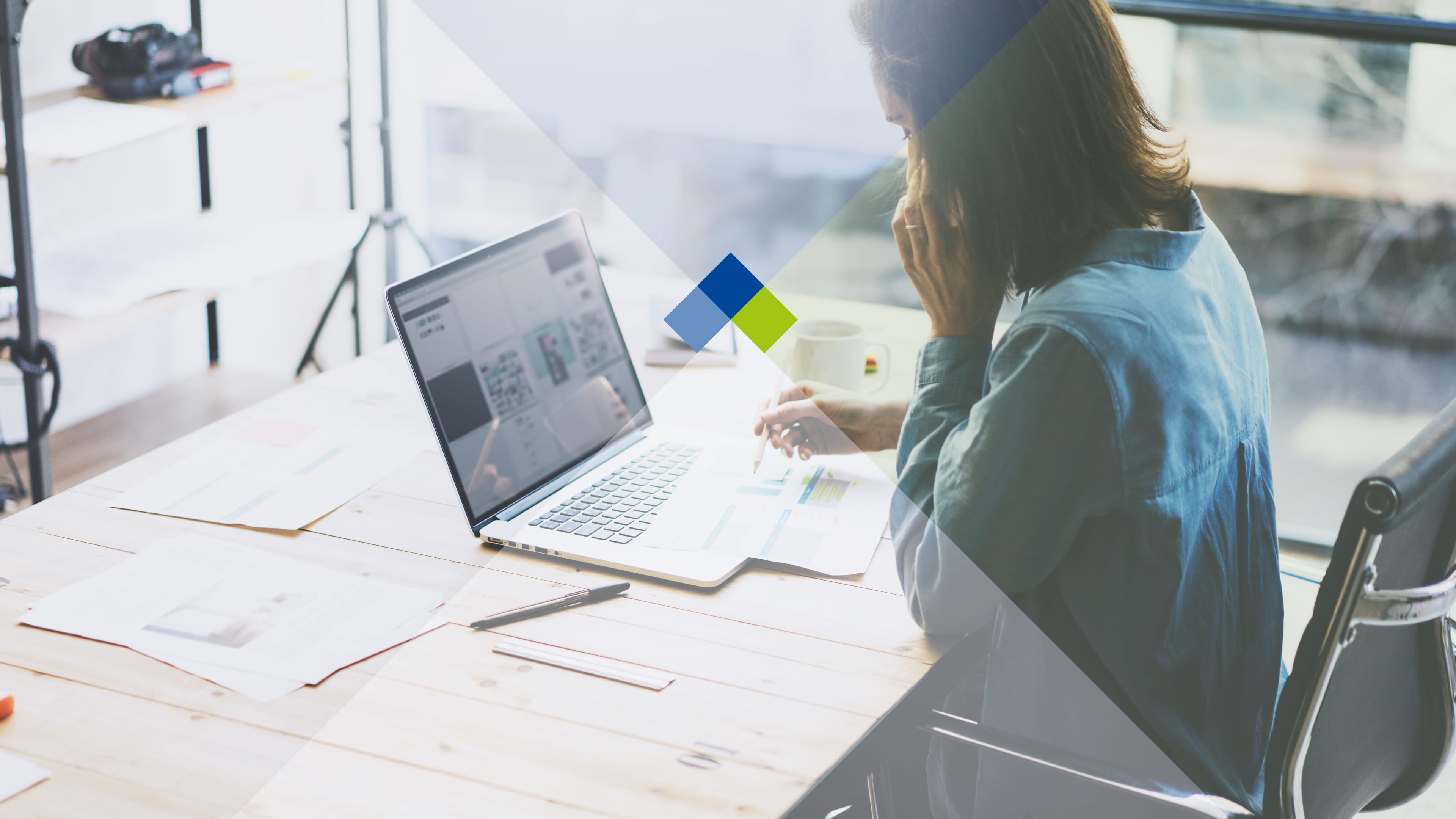 Weibliche Person sitzt mit offenem Laptop an einem Arbeitstisch