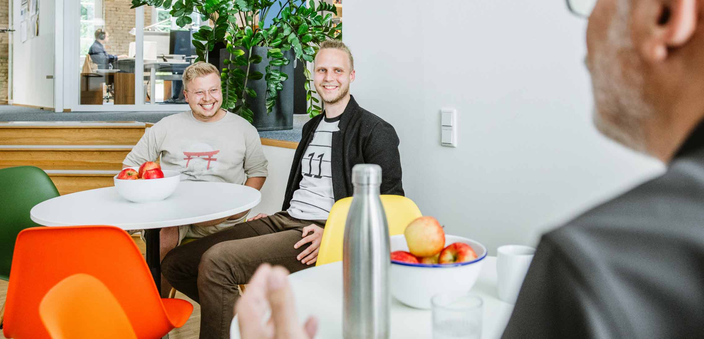 h2_werIst_teaser_03.jpg Drei Angestellte von Hochzwei in ihrer Mittagspause an zwei Esstischen.