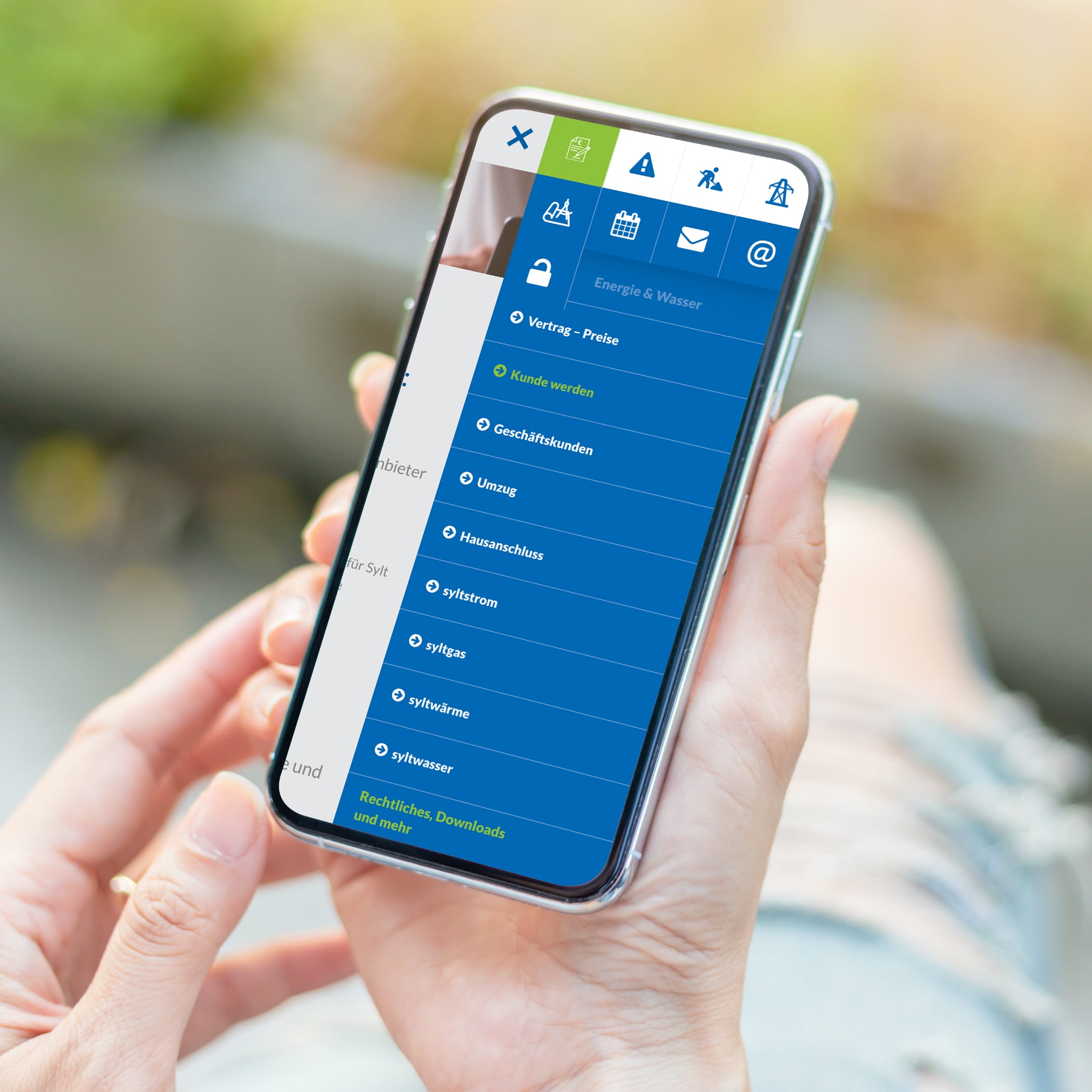 hochzwei_evs_teaser_05.jpg Hand hält Smartphone, das blaues Menü der Website der Energieversorgung Sylt zeigt