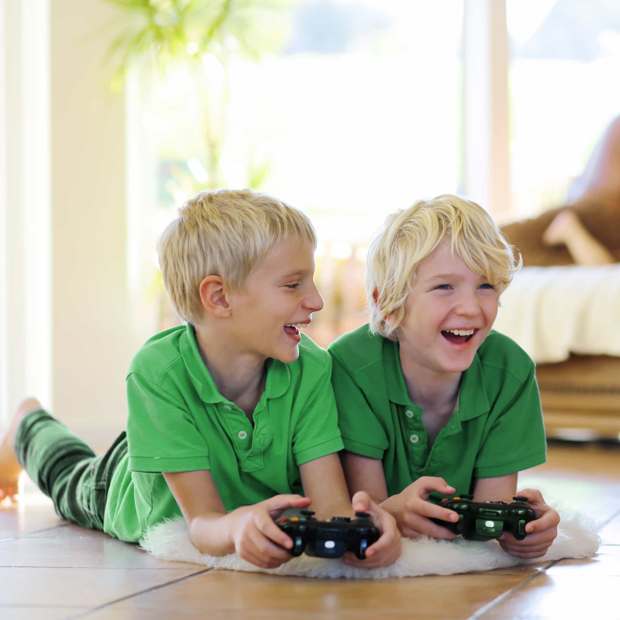 hochzwei_futura_teaser_04.jpg Zwei Kinder liegen in grünen Shirts auf dem Boden und spielen Playstation