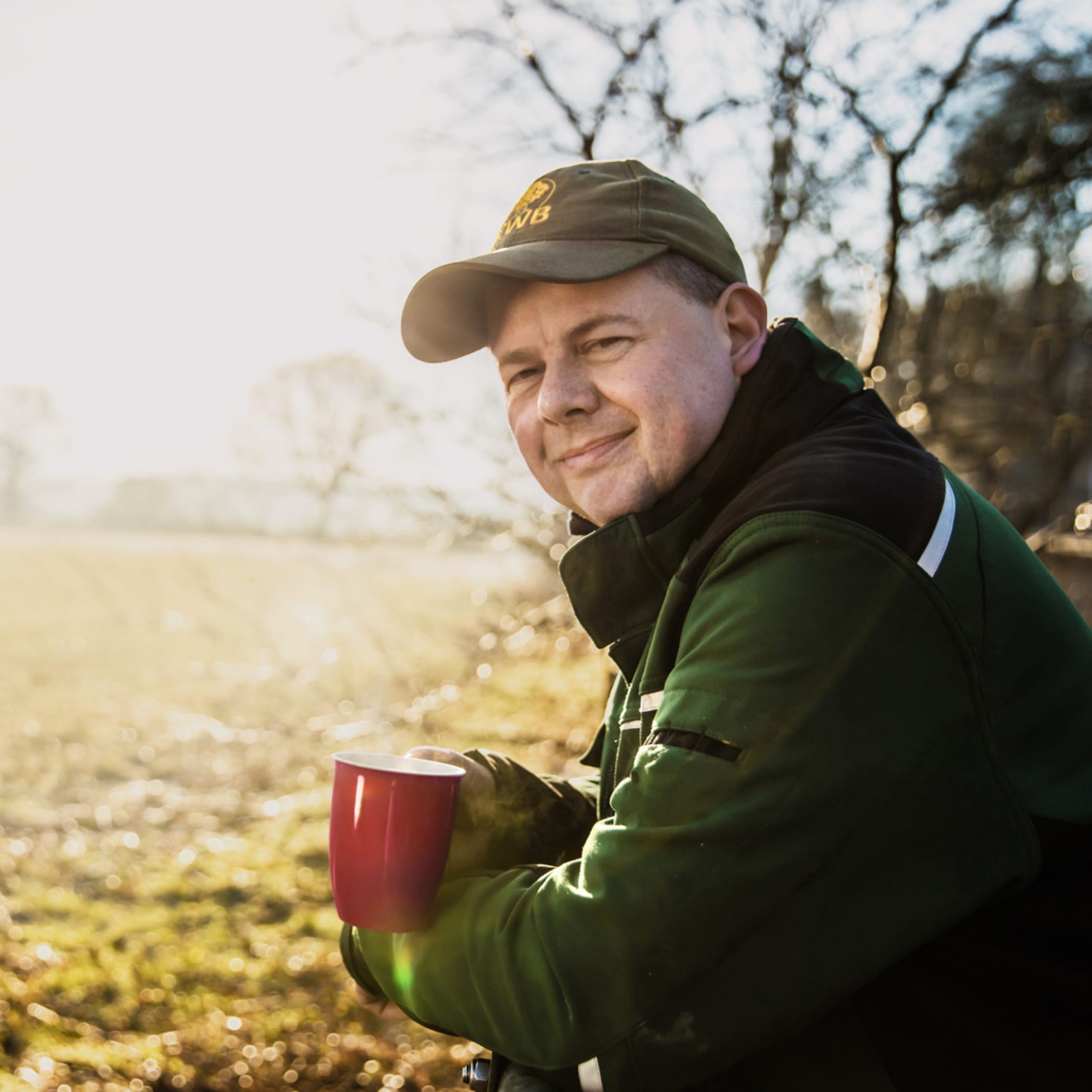Ein Mann lehnt sich an einen Zaun und hält eine rote Tasse