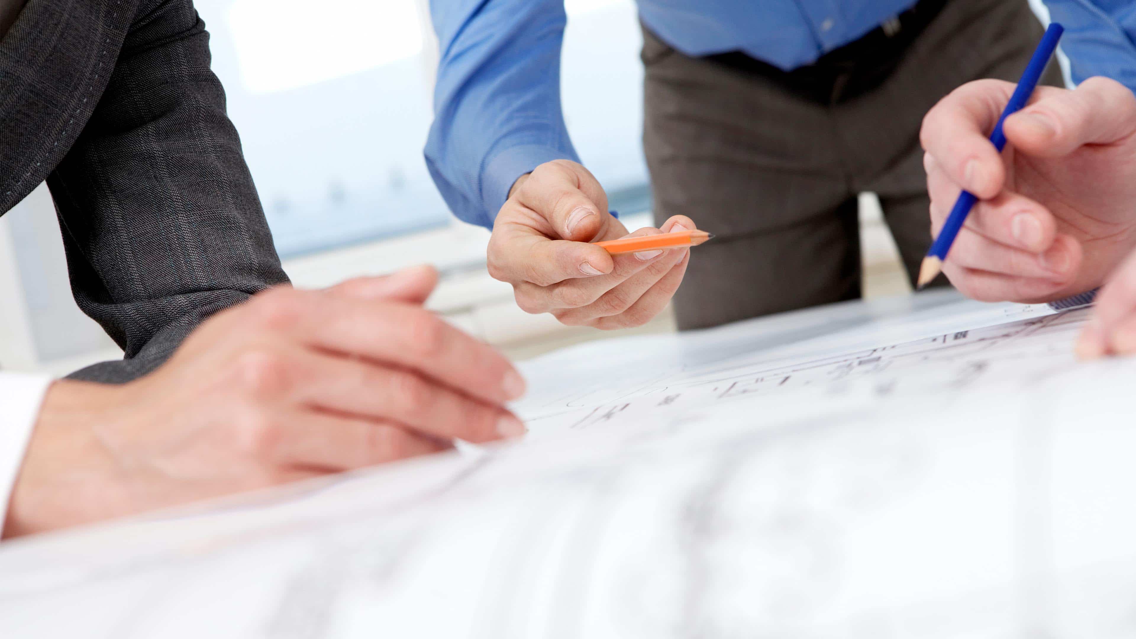 hochzwei_gottburg_slider_02.jpg Drei Personen zeichnen mit einem Bleistift auf einem Bauplan