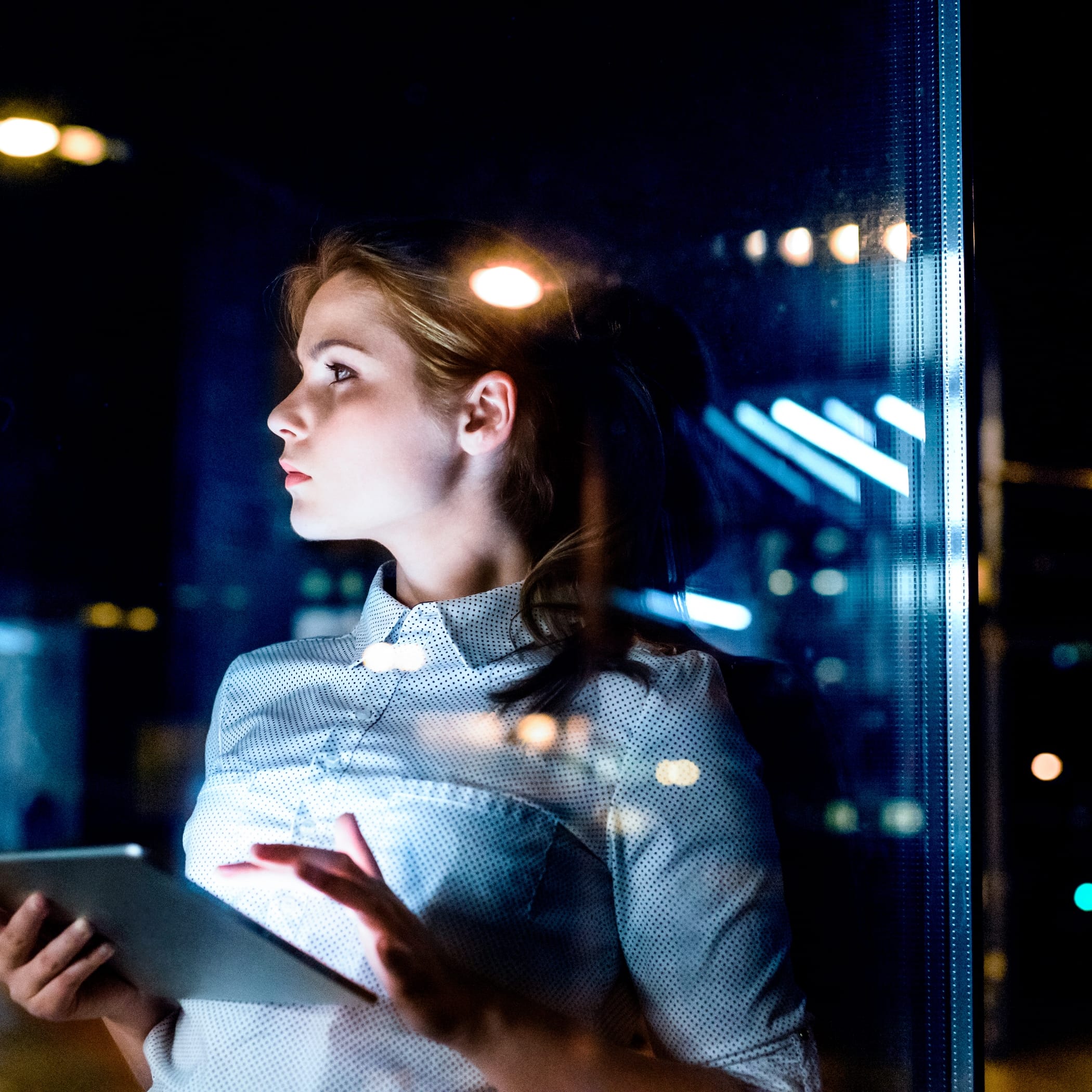 hochzwei_neoma_teaser_04.jpg Eine Frau steht Nachts am Fenster und hält nachdenklich ein Ipad in der Hand