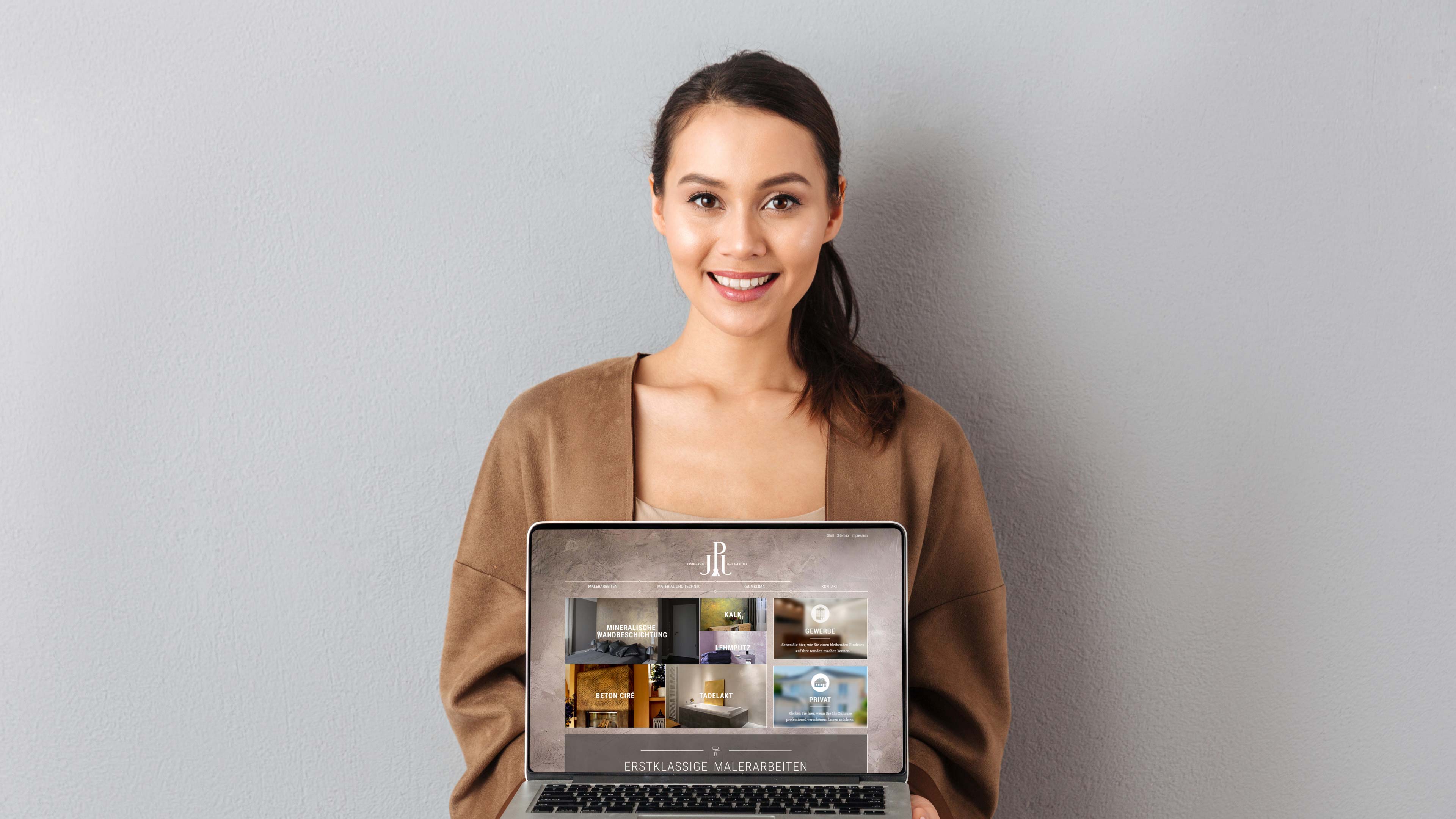 hochzwei_jpj_slider_02.jpg Eine dunkelhaarige Frau hält einen Laptop und lächelt in die Kamera