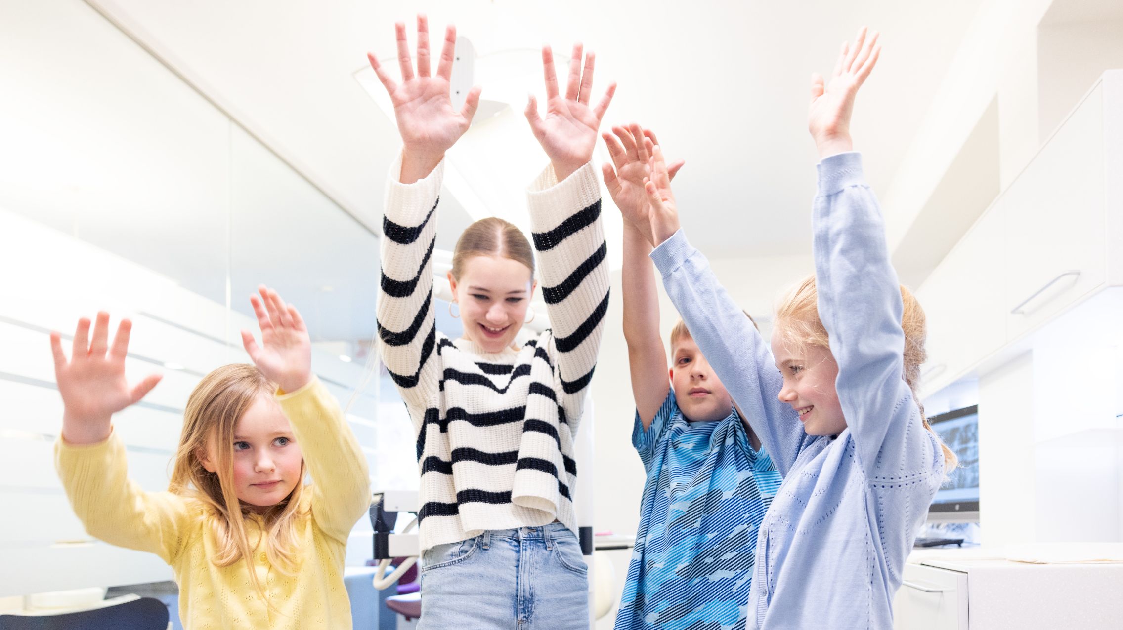Vier spielende Kinder in der Praxis, die beide Hände in die Luft strecken