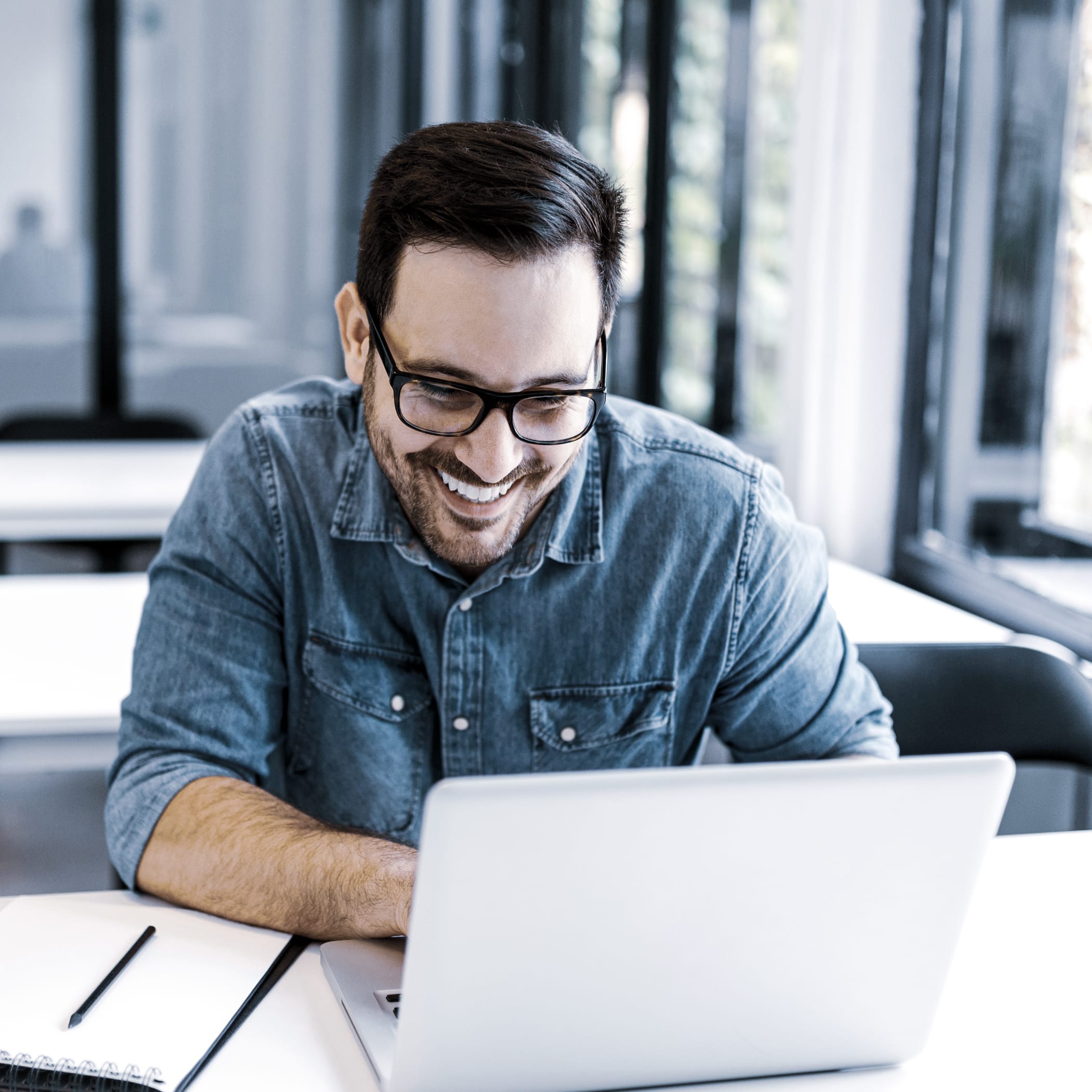 hochzwei_knpushbox_teaser_03.jpg Brünetter Mann im Hemd lächelt auf seinen Laptop Bildschirm