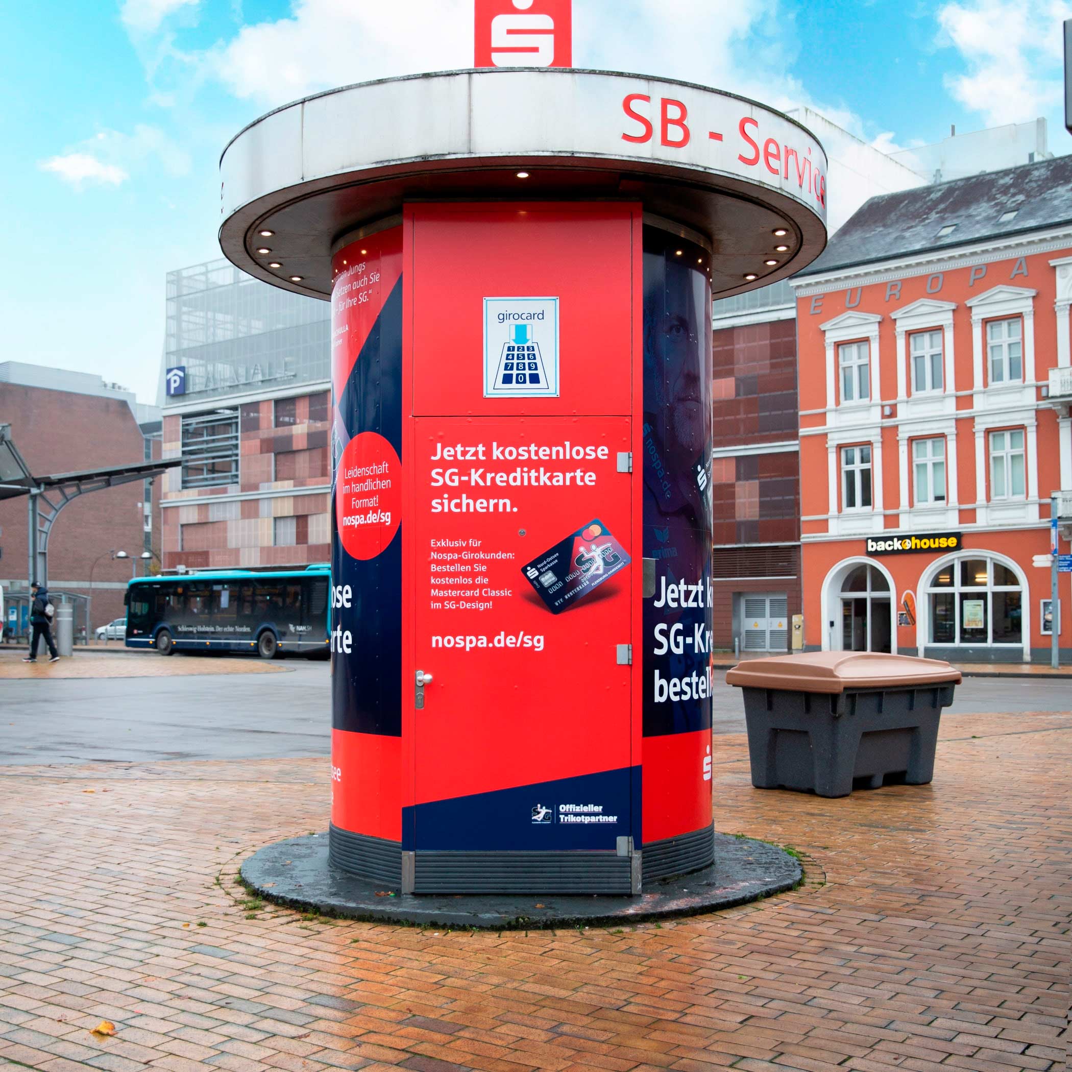 hochzwei_sgkreditkarte_teaser_10.jpg Werbeplakat auf einer Säule mit einem Sparkassen Automaten