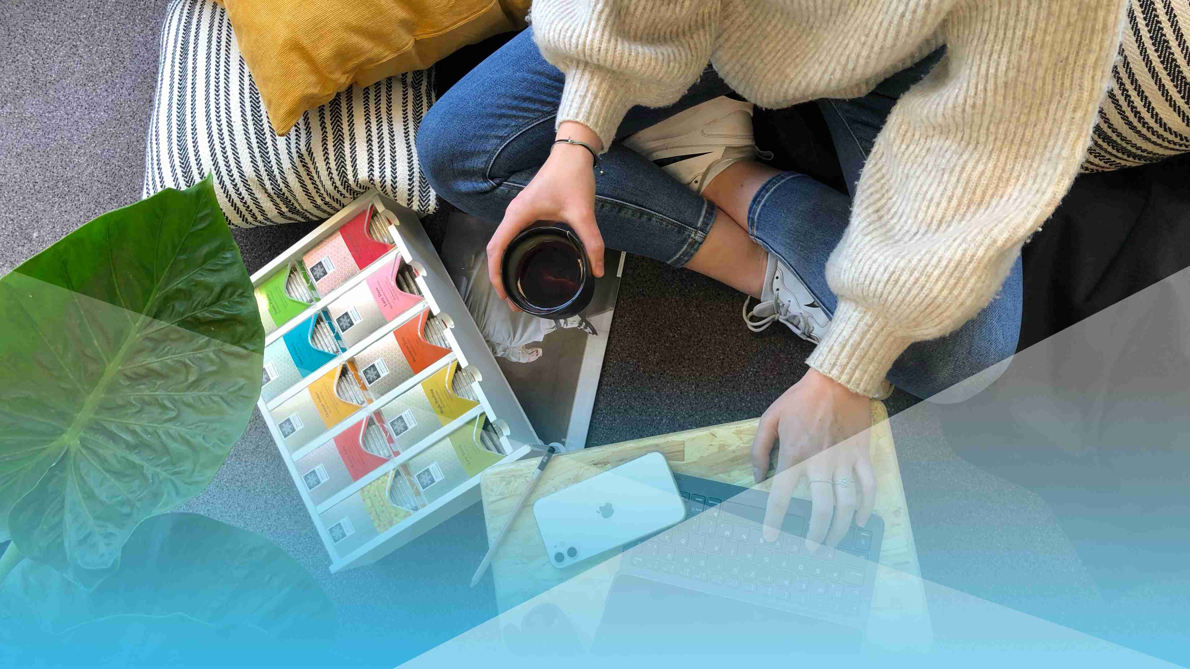 Eine Jugendliche sitzt mit ihrer Teetasse auf dem Boden. Neben ihr eine Teebox, ein Laptop und ihr Handy.