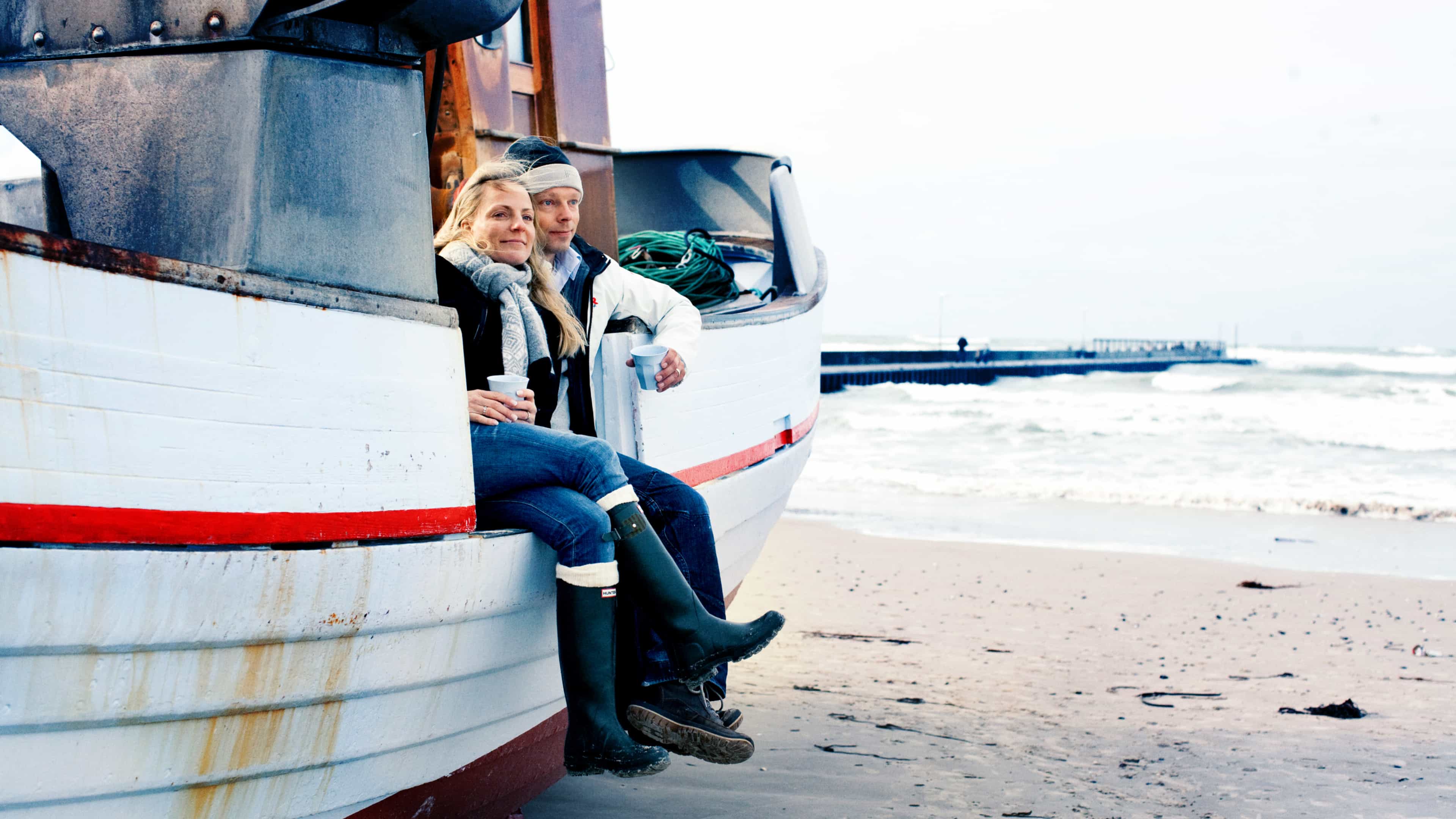 Frau und Mann sitzen in einem gestrandeten Boot am Meer