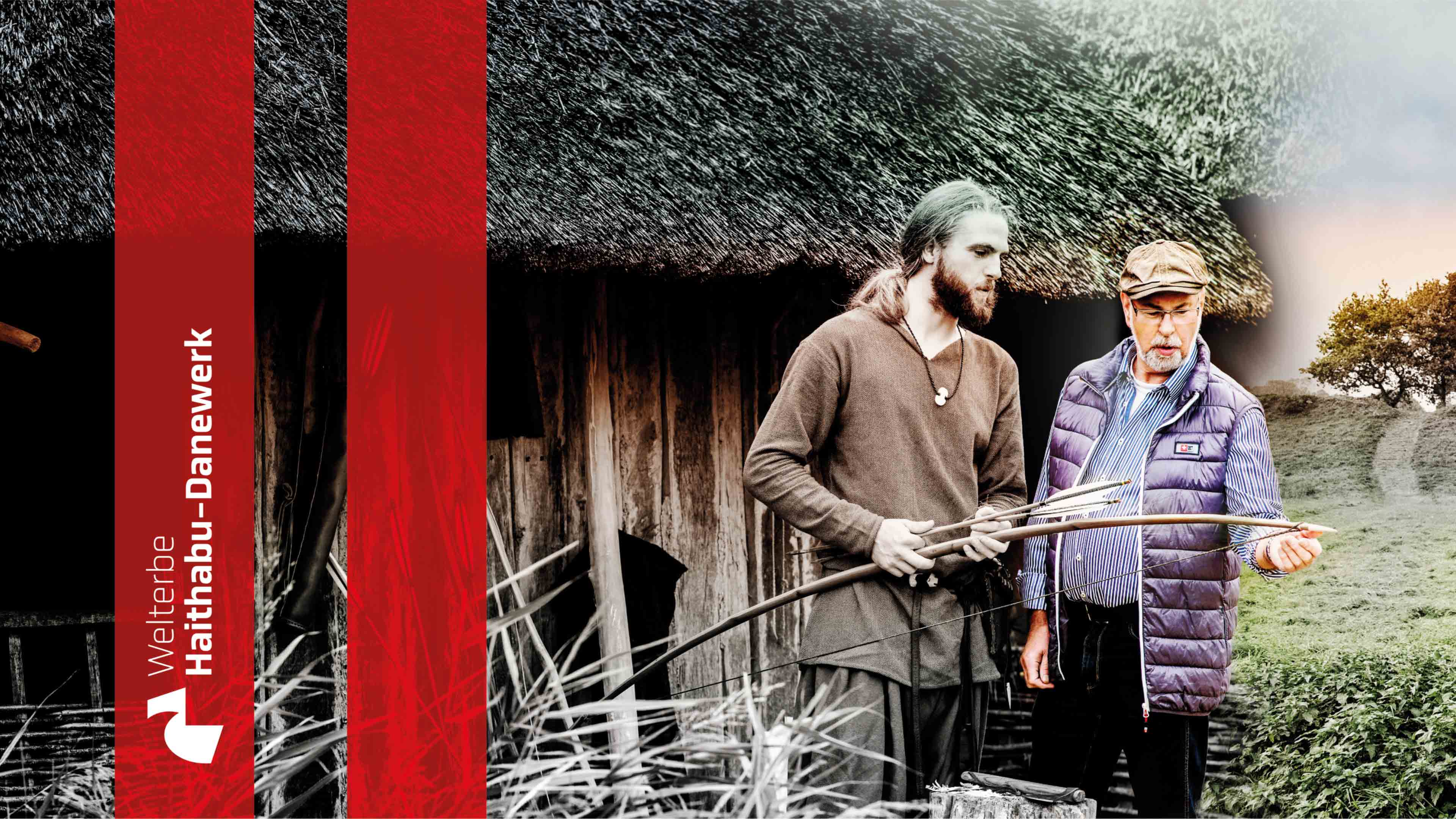 Stehend vor einem reetgedeckten Gebäude schaut ein moderner Mann auf Pfeil und Bogen in der Hand eines Mannes in Wikingerkluft