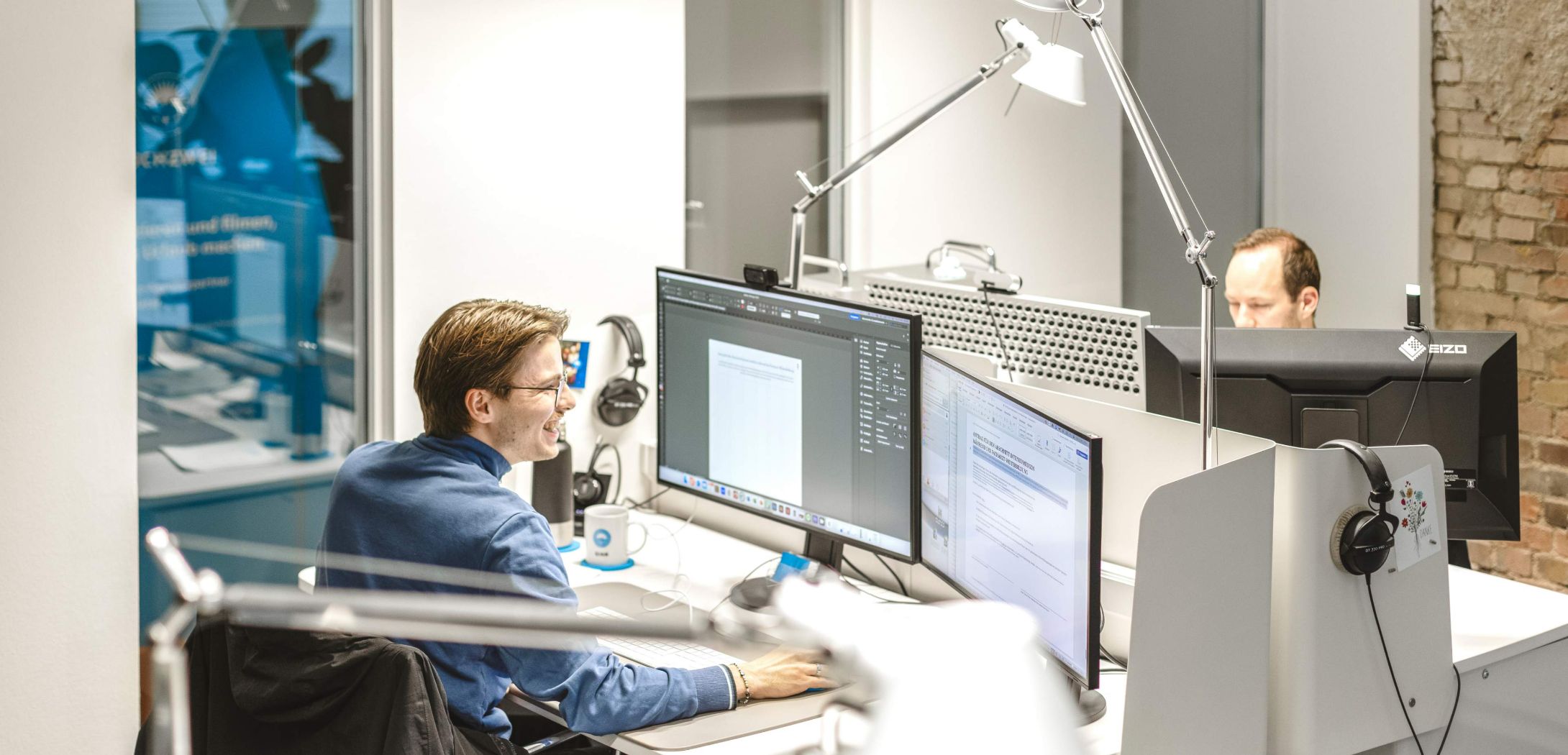 Zwei gegenüberliegende Arbeitsplätze mit Pc an denen jeweils eine Person sitzt